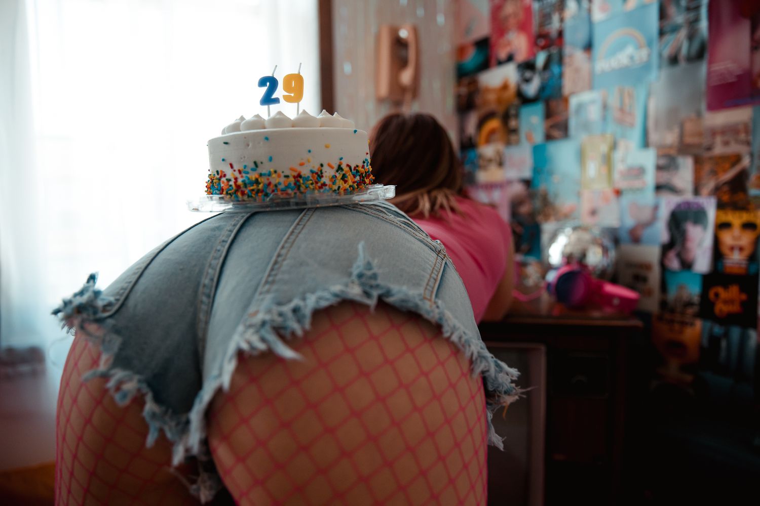 Person leaning over a birthday cake with a 29 candle in a decorated bedroom.