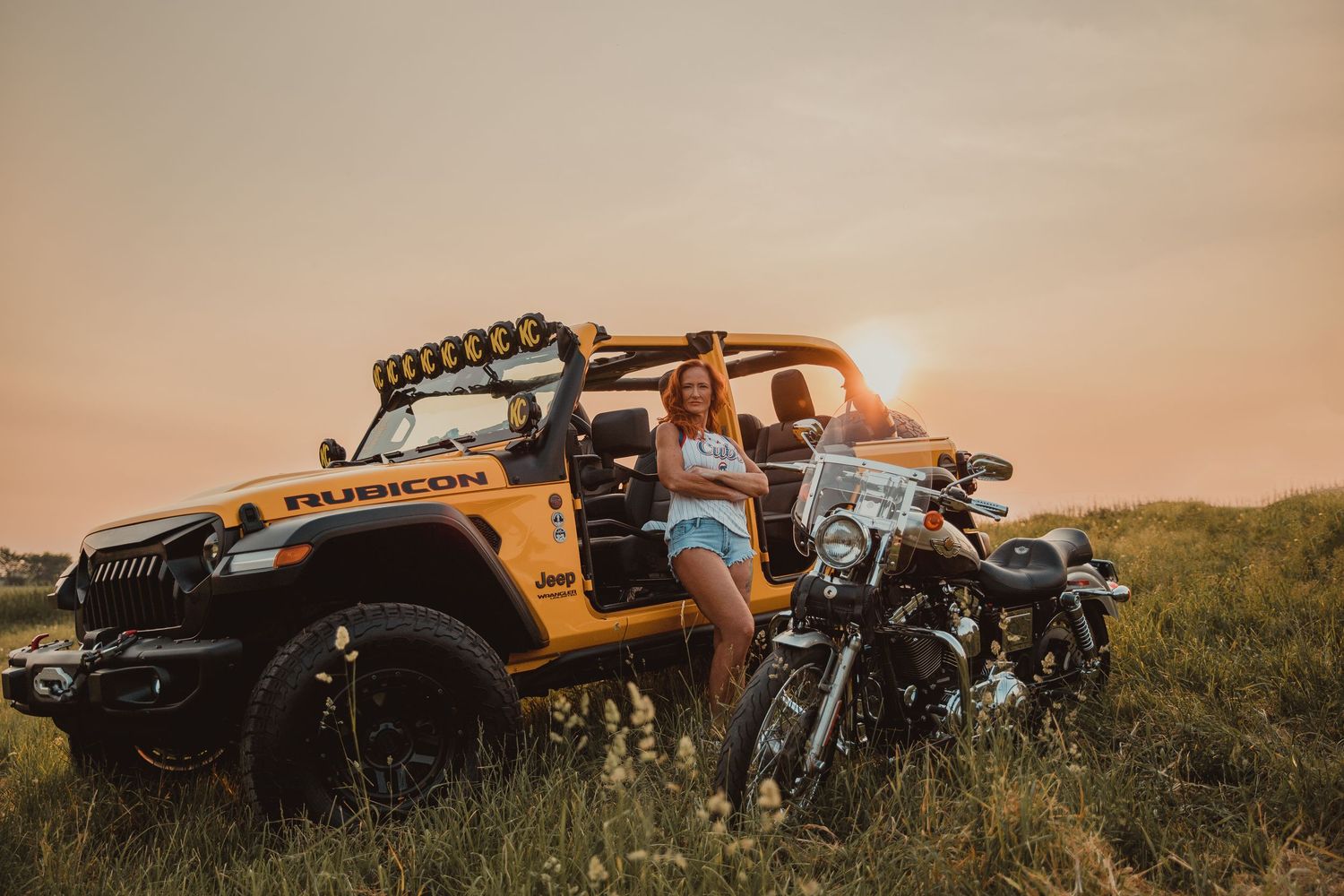 Yellow off-road vehicle and motorcycle parked in grassy field at sunset with a warm golden sky backdrop.