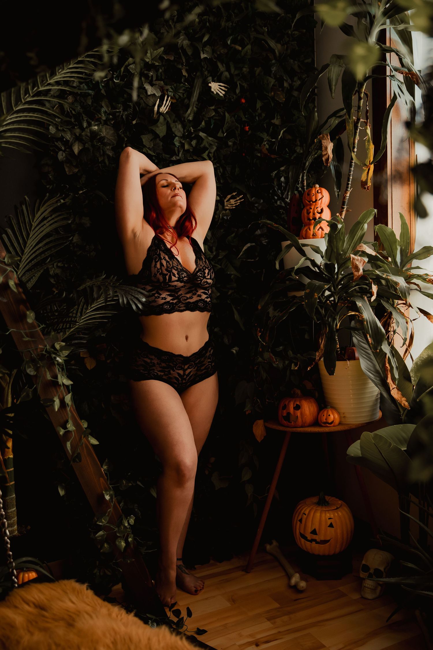 Moody Halloween boudoir photoshoot scene with pumpkins, tropical plants and dark romantic lighting.