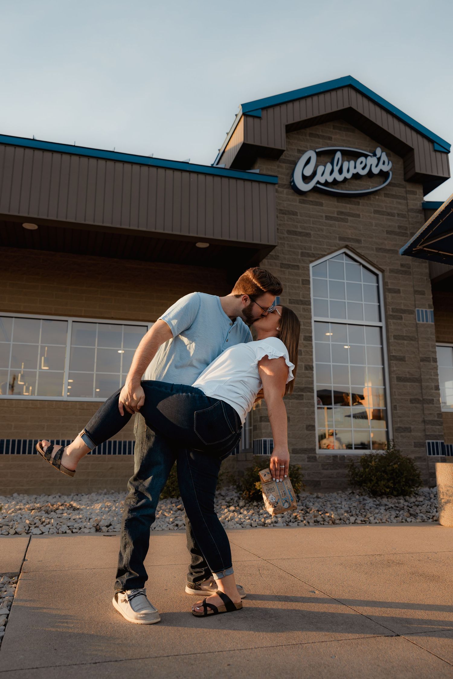 Couple sharing a romantic dip kiss outside a Culvers restaurant at sunset.