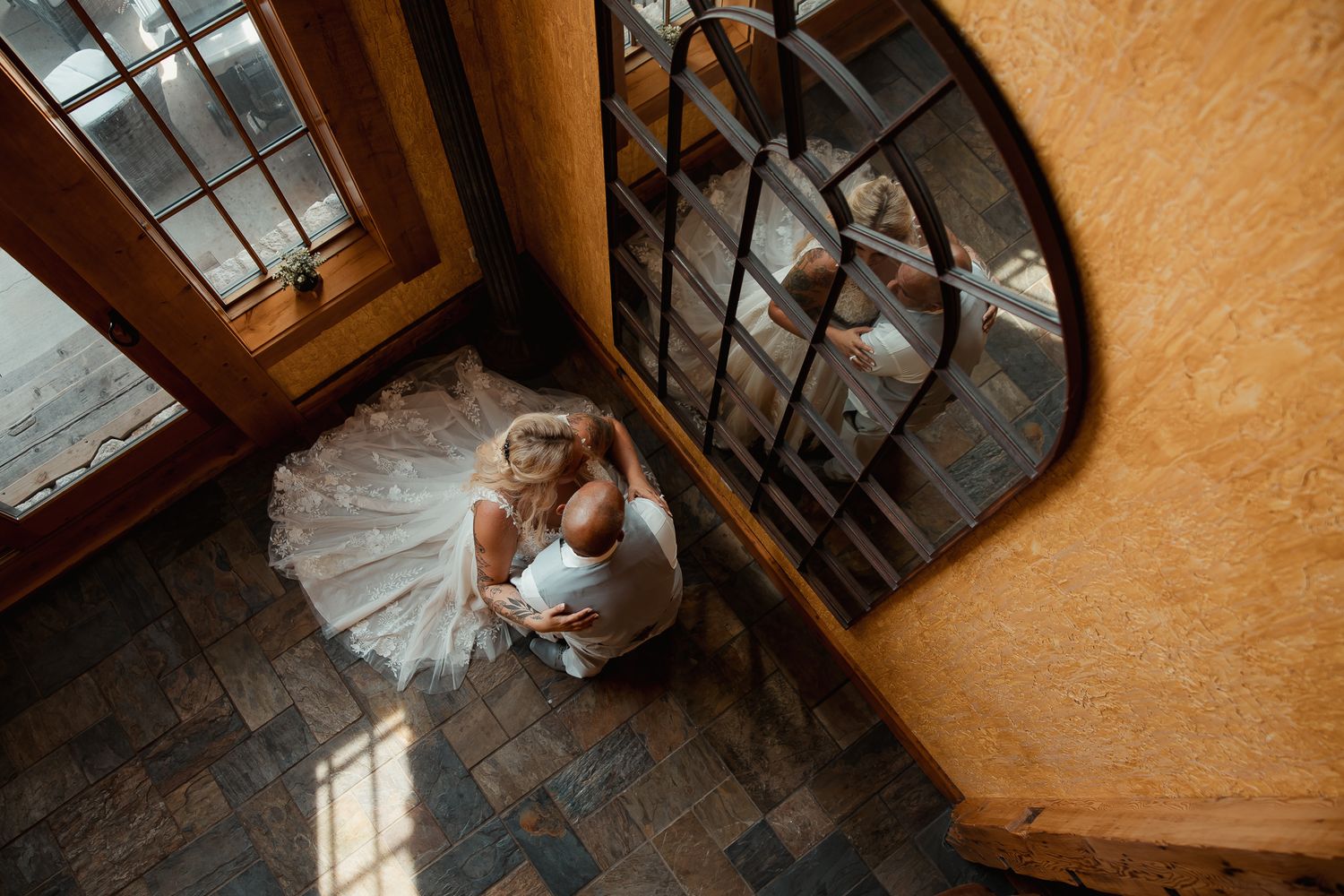 High angle view of a bride in a white tulle dress sitting on rustic dark wood floor by a vintage window.