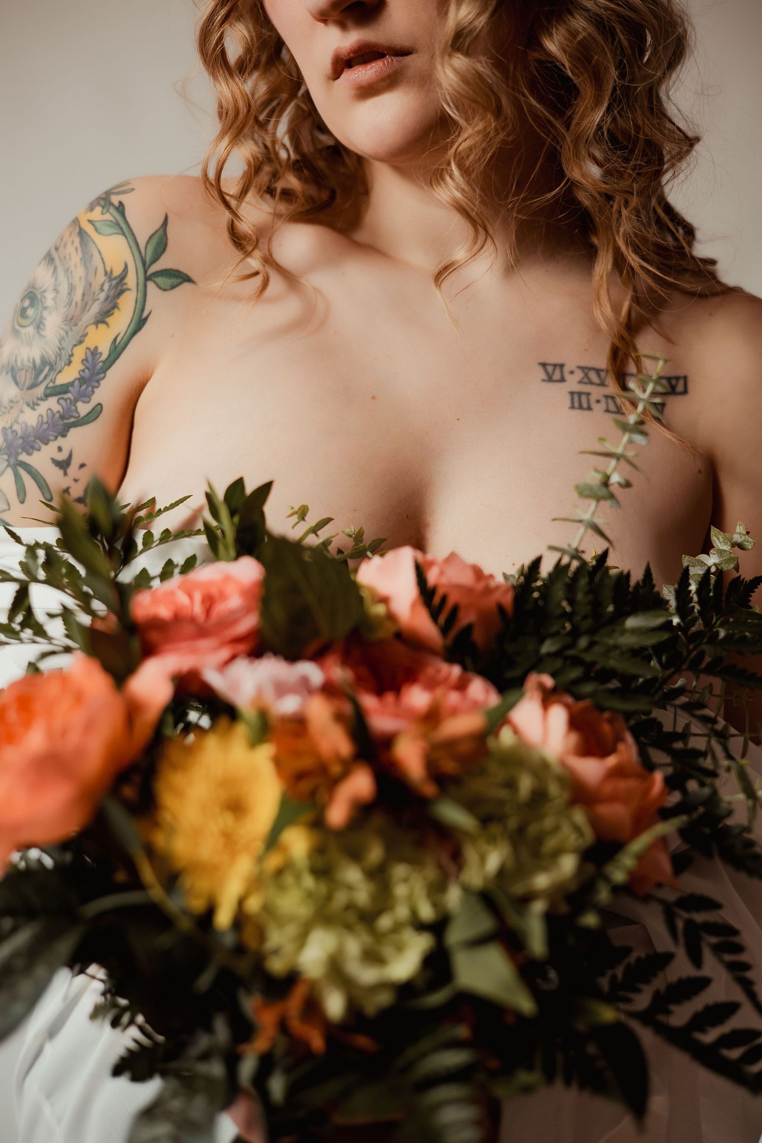 Artistic bridal portrait featuring peach and yellow roses with visible floral tattoo artwork and curled hair.