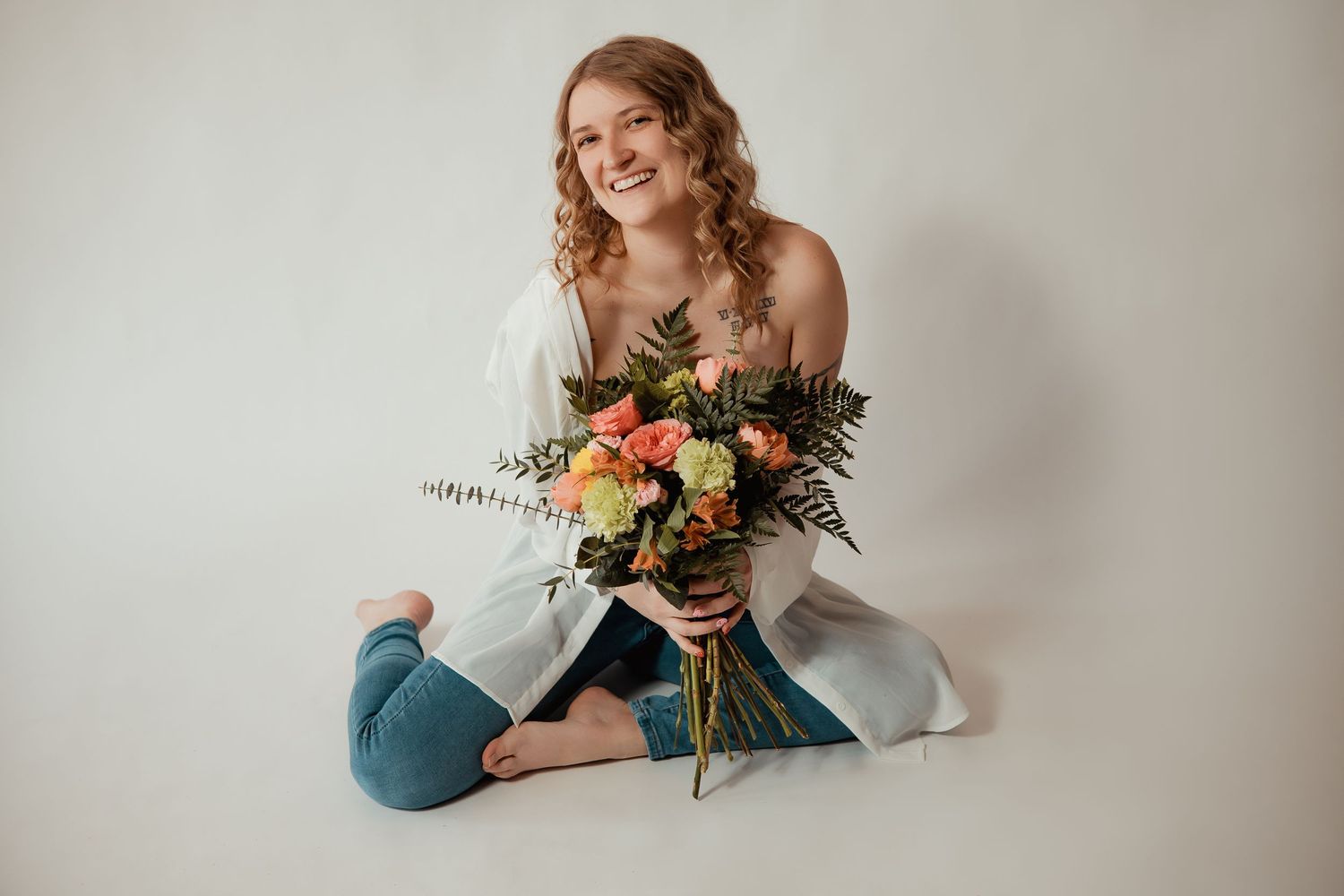 A person in a white wedding dress sits gracefully on a light backdrop holding a colorful floral bouquet.