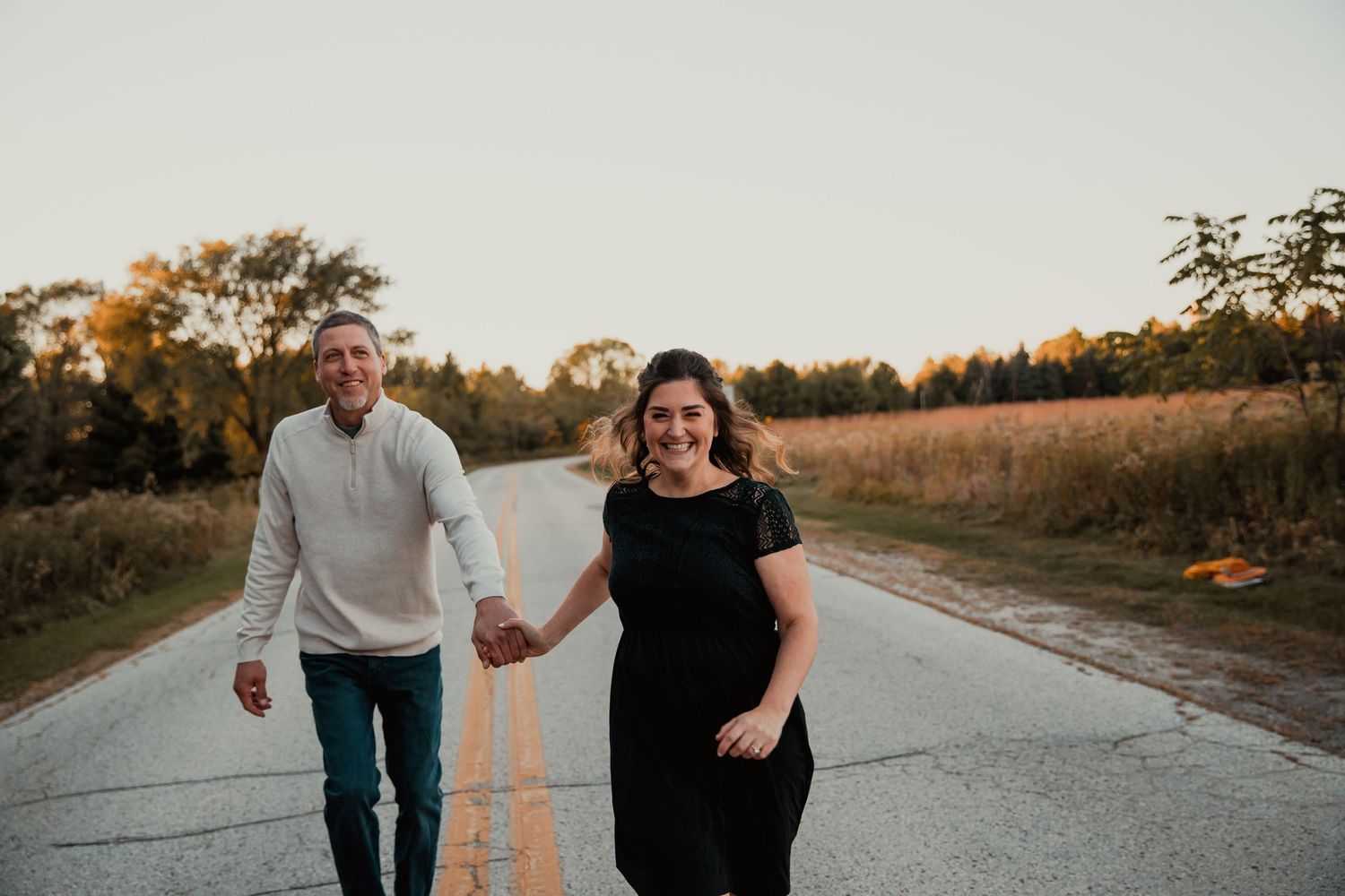 A couple holds hands while walking down a rural road at sunset. couples engagement