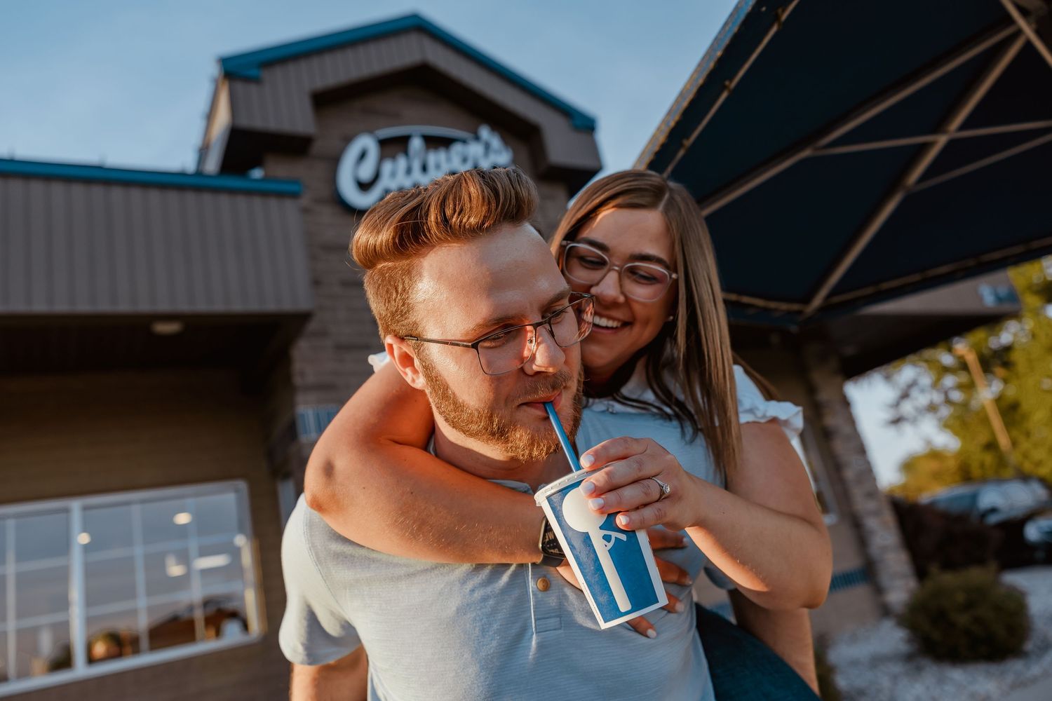 Happy couple hugging outside Culver's restaurant, sharing a blue drink on a sunny day.