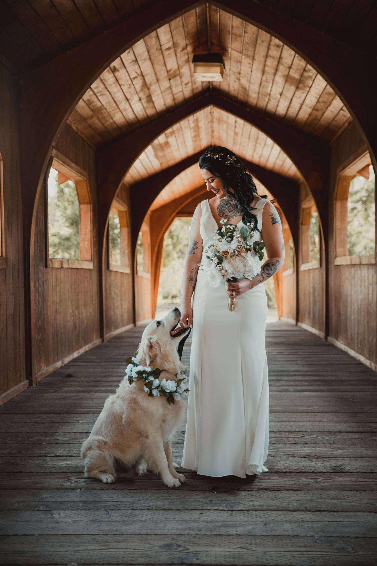 A bride in a white gown poses with her golden retriever in a wooden covered bridge. wedding