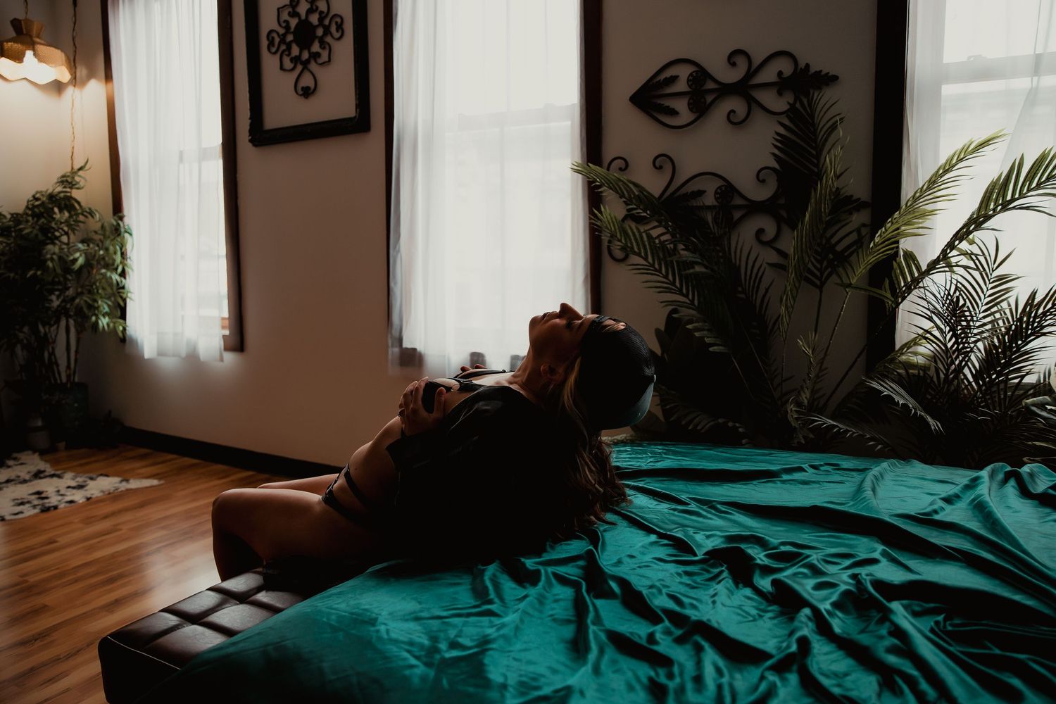 A cozy bedroom interior with emerald green bedding and natural light streaming through white curtained windows.