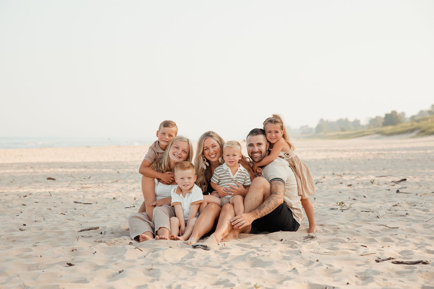 Family group poses together on sandy beach during sunset photo session.