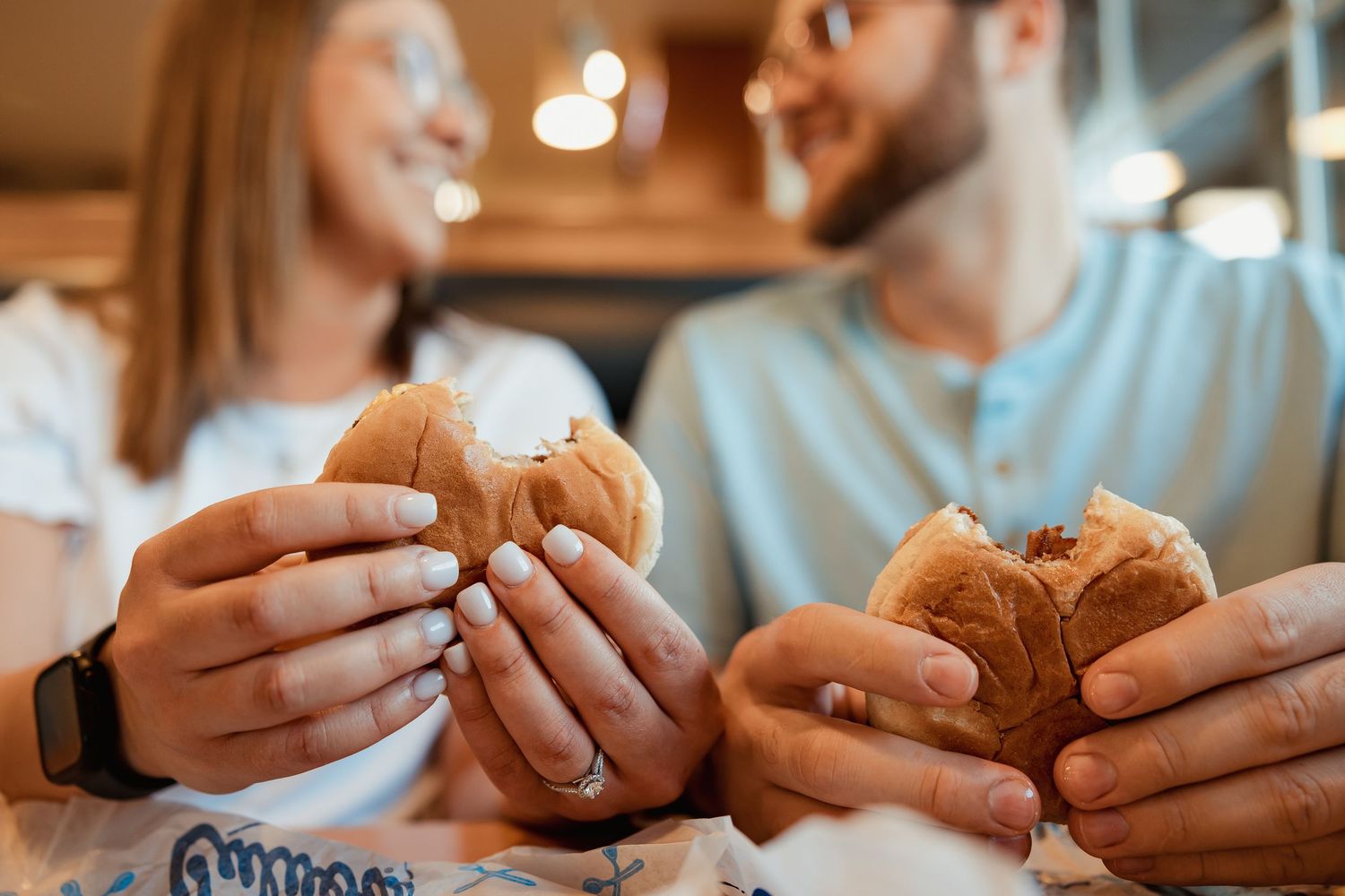 A smiling couple holding burgers together at a Culvers fast food restaurant on a date.