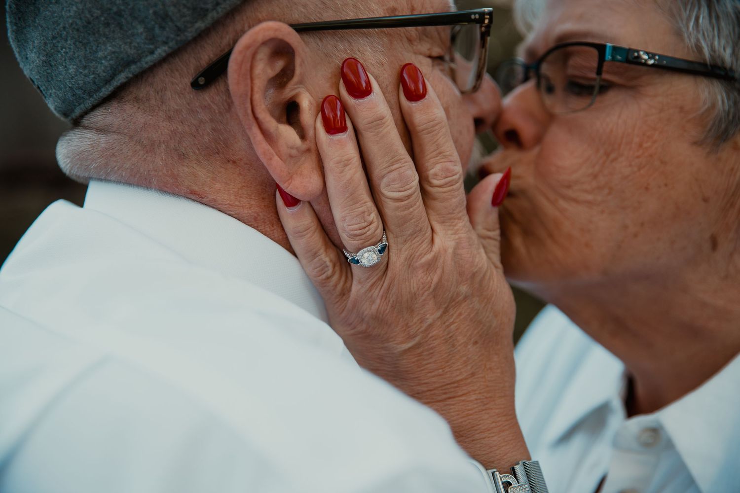 Intimate close-up of couple kissing with red nail polish visible on hand. couples engagement
