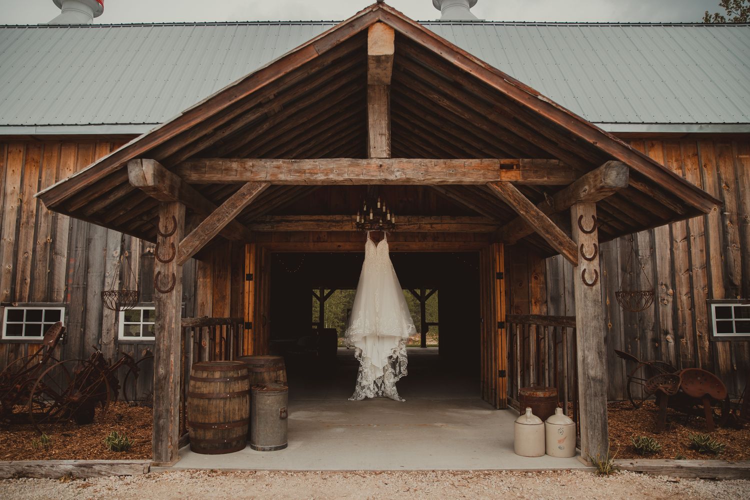 A wedding dress hangs in a rustic wooden barn entrance framed by timber beams. wedding