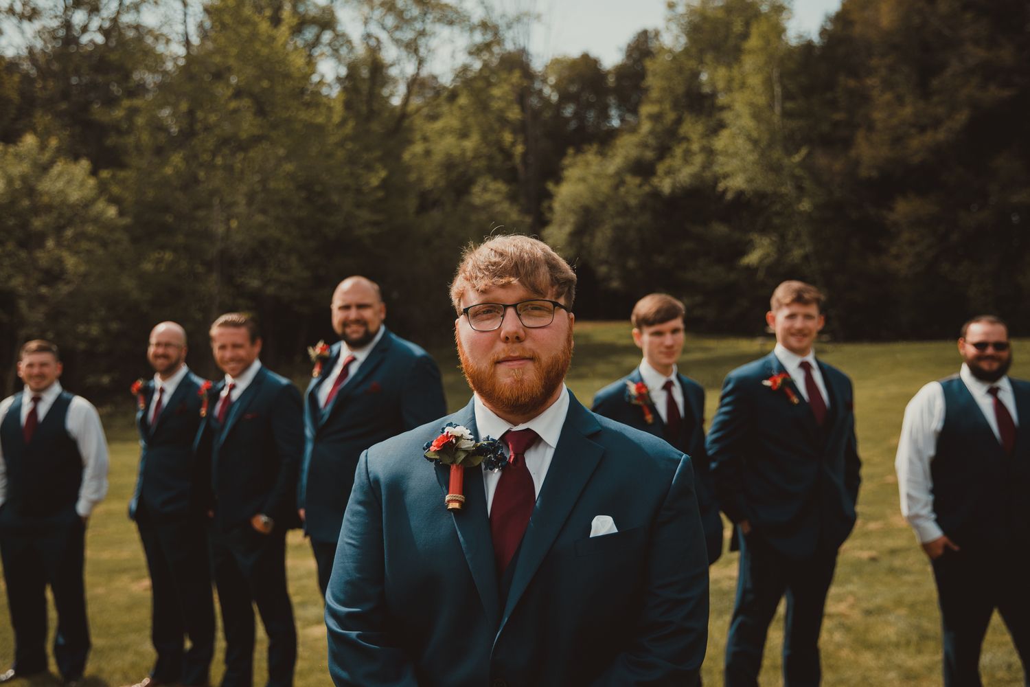 Wedding party poses outdoors with groomsman in blue suit standing in foreground. wedding