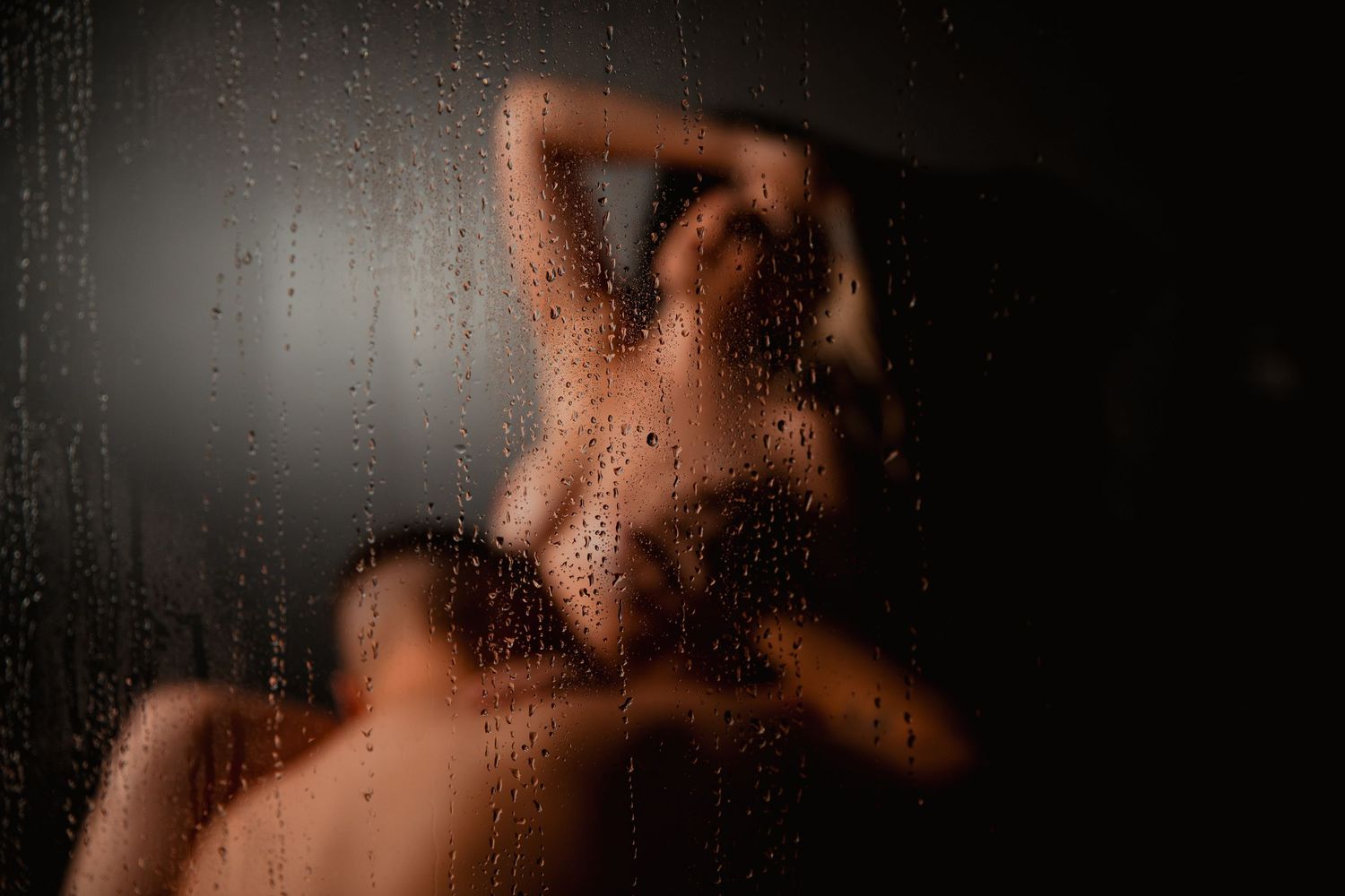 Silhouetted figure behind steamy glass with water droplets creating a moody, intimate atmosphere.