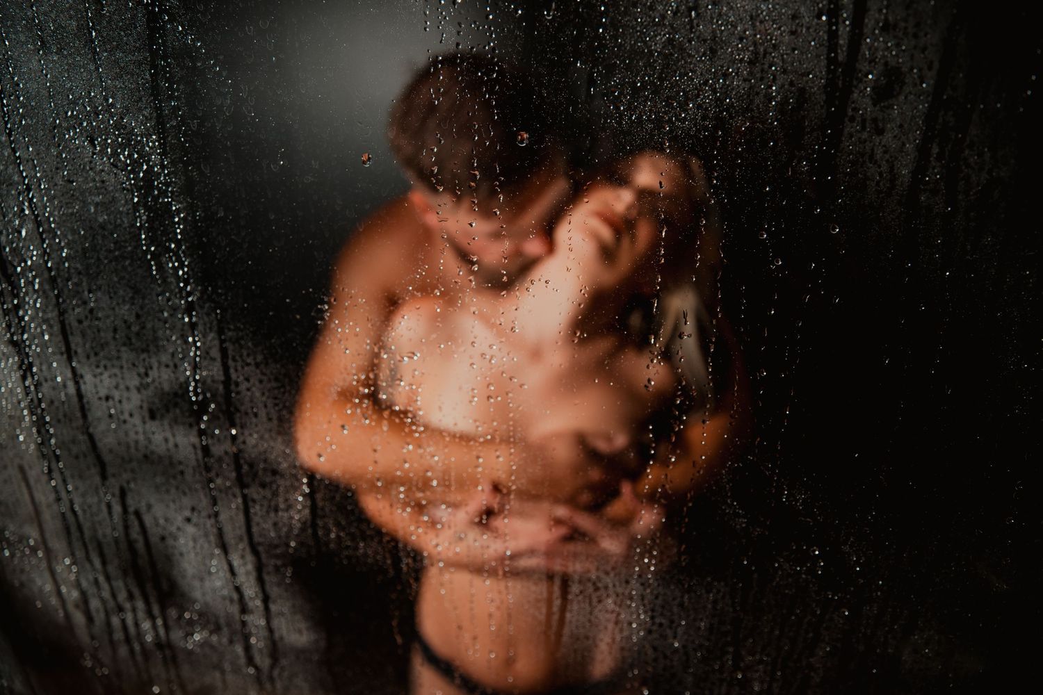 Artistic silhouette of a couple embracing behind steamy glass with water droplets creating a moody atmosphere.
