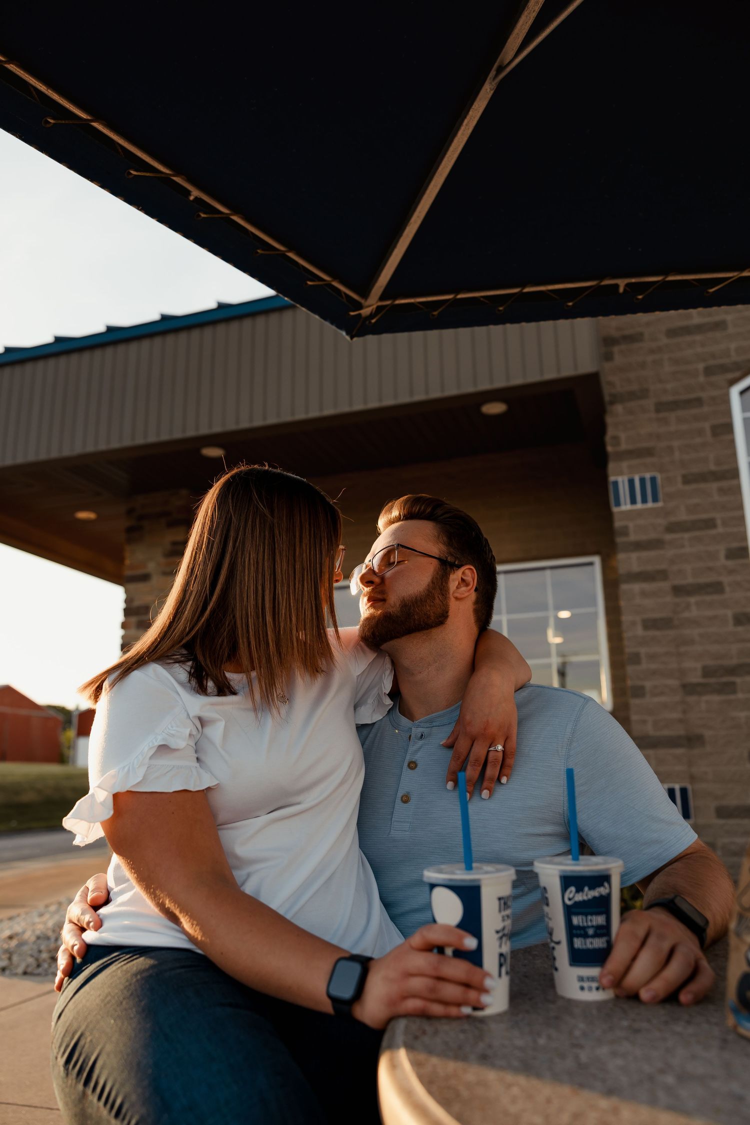 Couple sharing a romantic moment at Culver's outdoor patio at sunset, embracing with frozen custard drinks nearby.