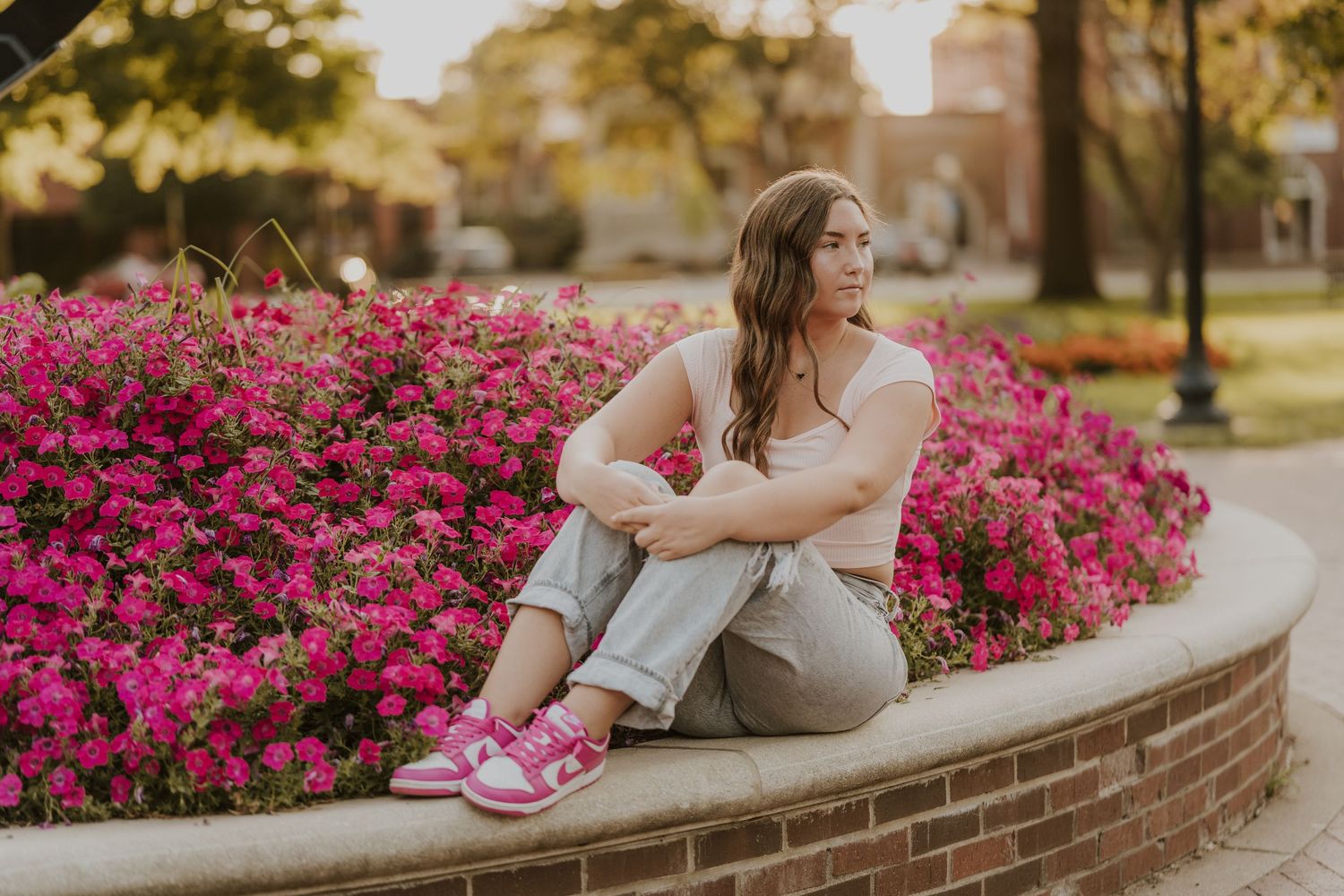 A springtime senior portrait session by vibrant pink flowers on a brick garden wall at sunset.