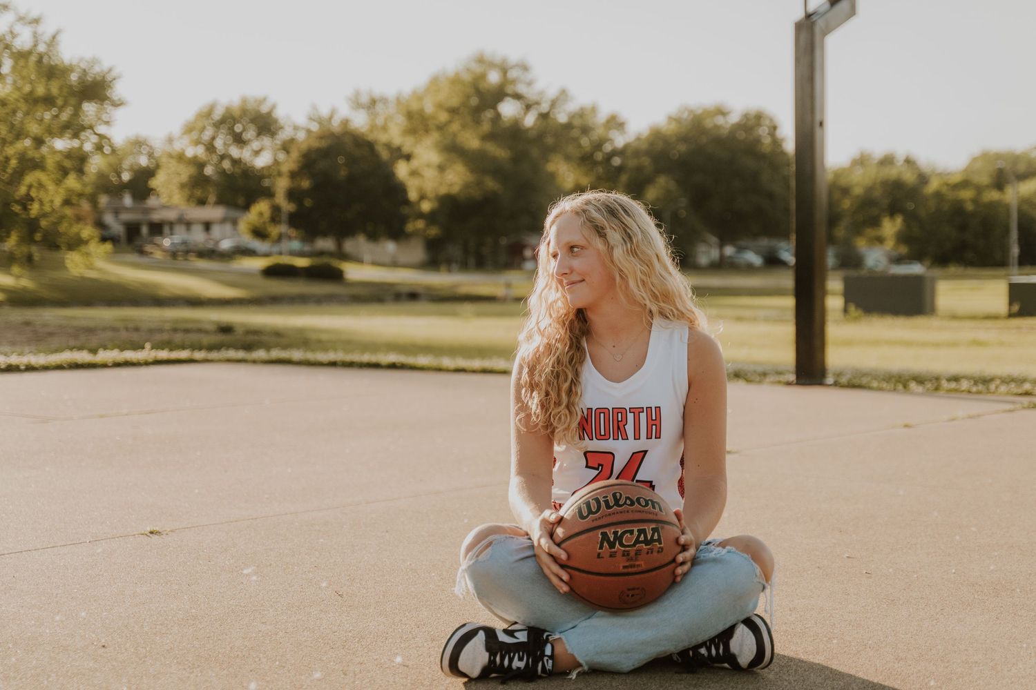 An outdoor sports-themed senior portrait with basketball and casual athletic wear in golden evening light.