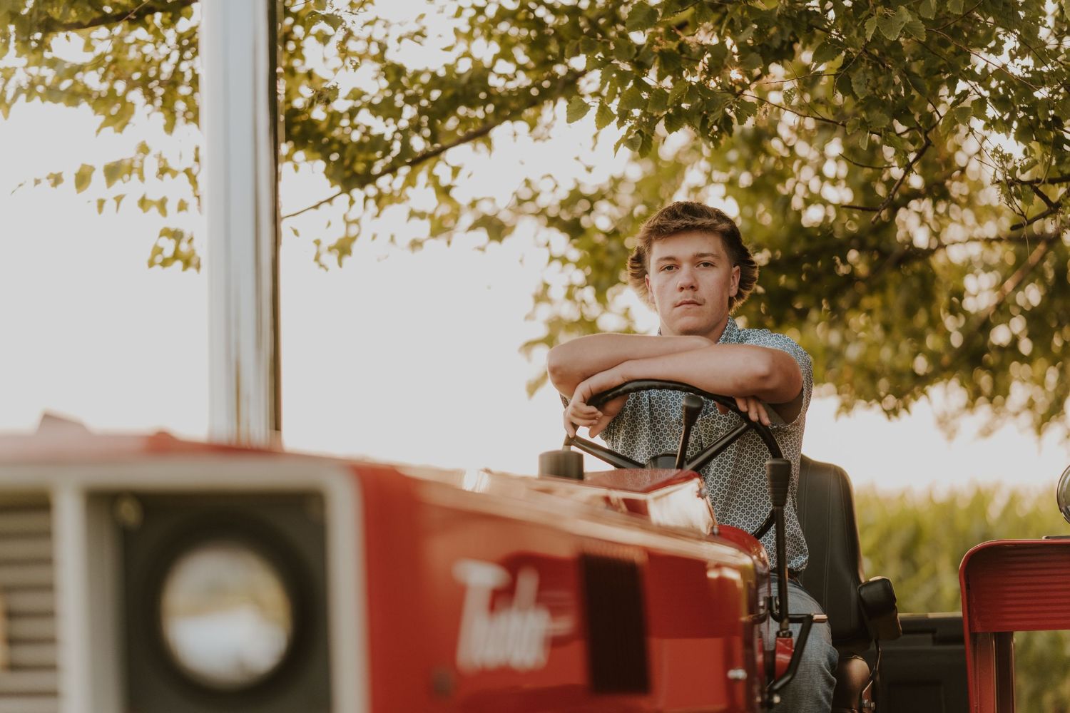 A vintage-style senior portrait on a red tractor showcases rural farm life during sunset.