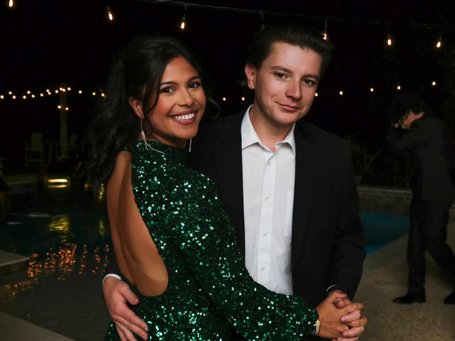 Guests in formal attire at an evening celebration with string lights in the background.