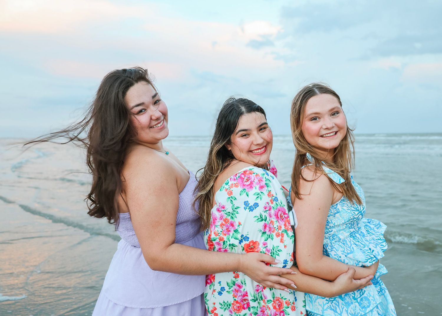 Friends in summer dresses share joyful moment together on beach at dusk.