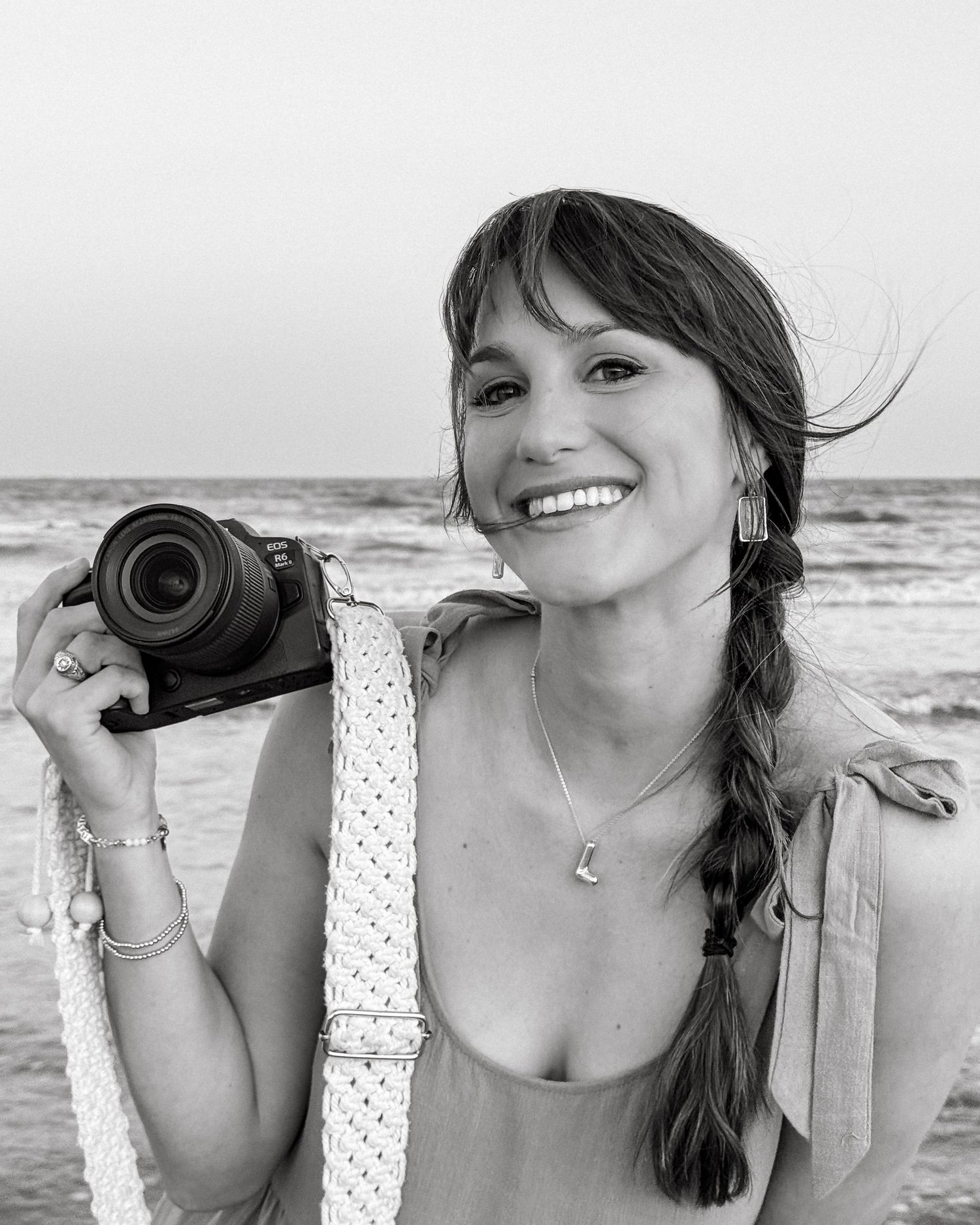 A series of black and white beach portraits showing someone posing with a camera against an ocean backdrop.