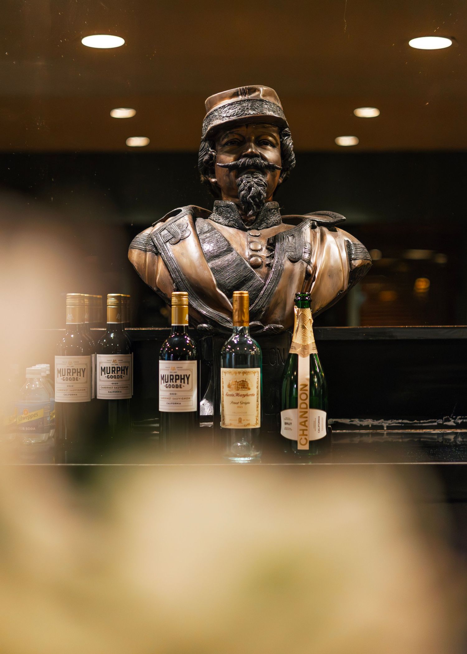 Row of whiskey bottles lined up on a dark bar shelf with overhead lighting creating a moody ambiance.