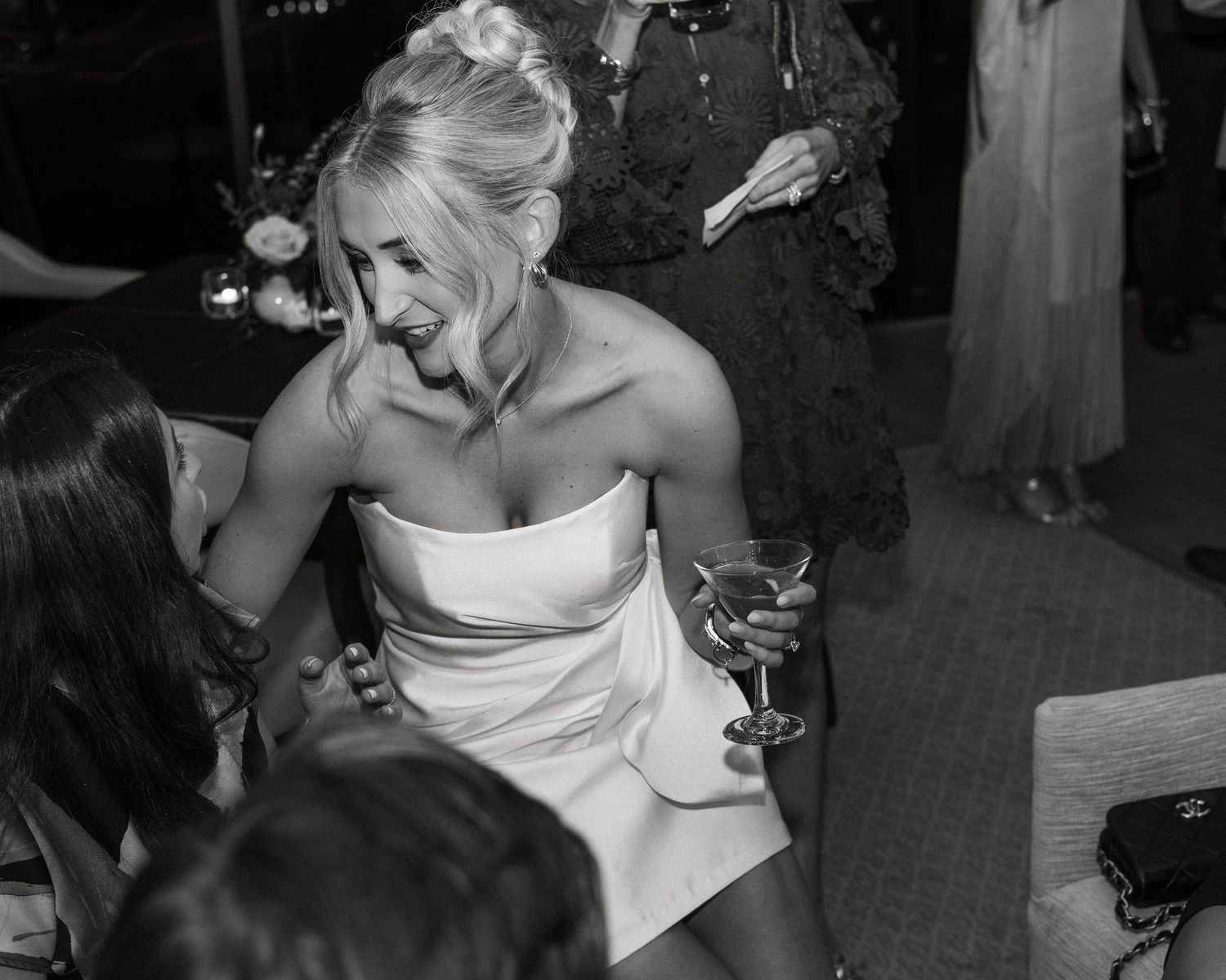 A candid black and white photo of a bride in a strapless white dress laughing during her wedding reception.