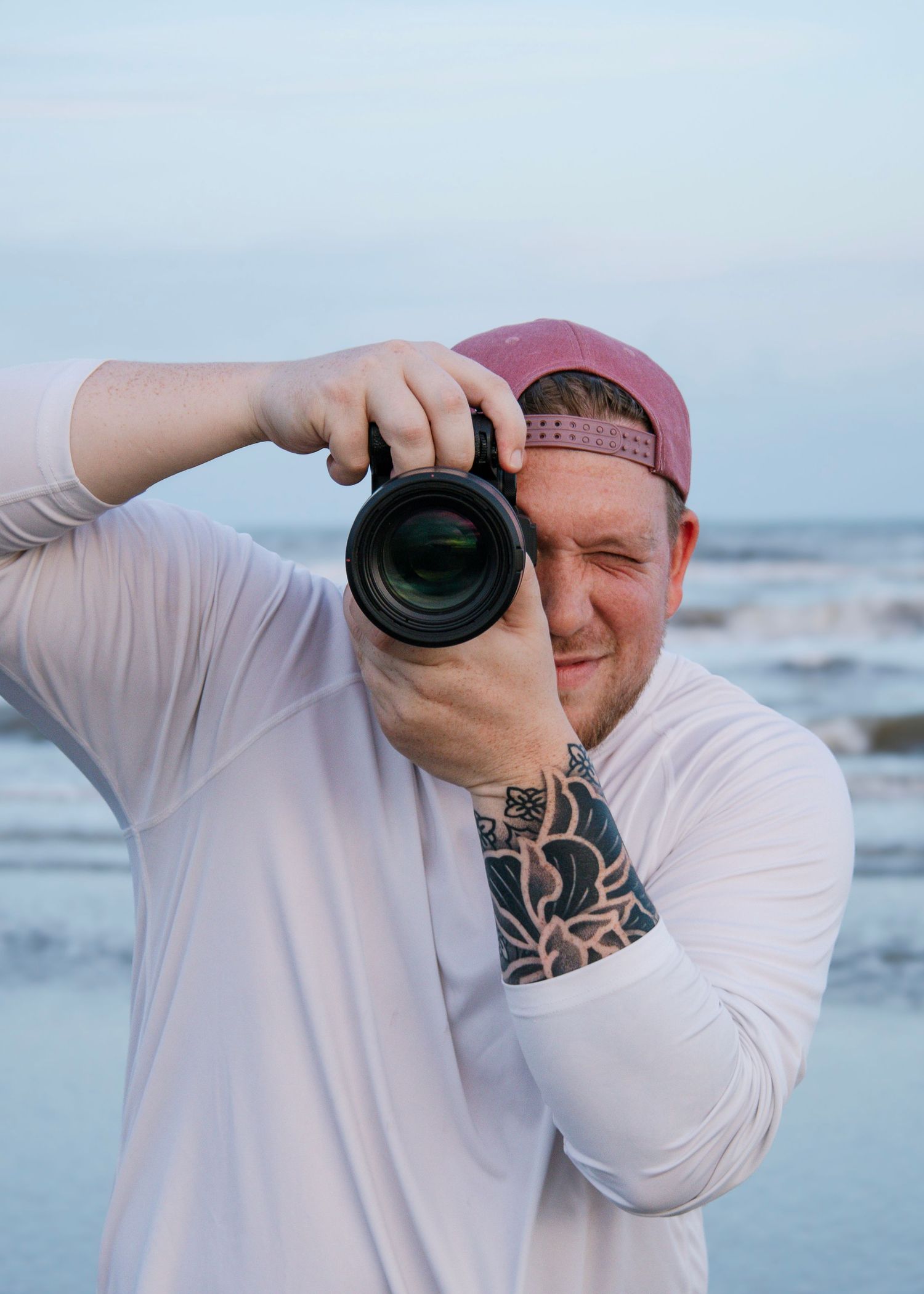 Photographer in white shirt taking pictures at a beach during overcast weather.