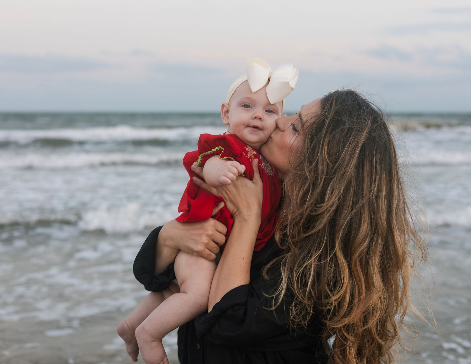 A tender moment shared between parent and child against a dramatic ocean backdrop at sunset.