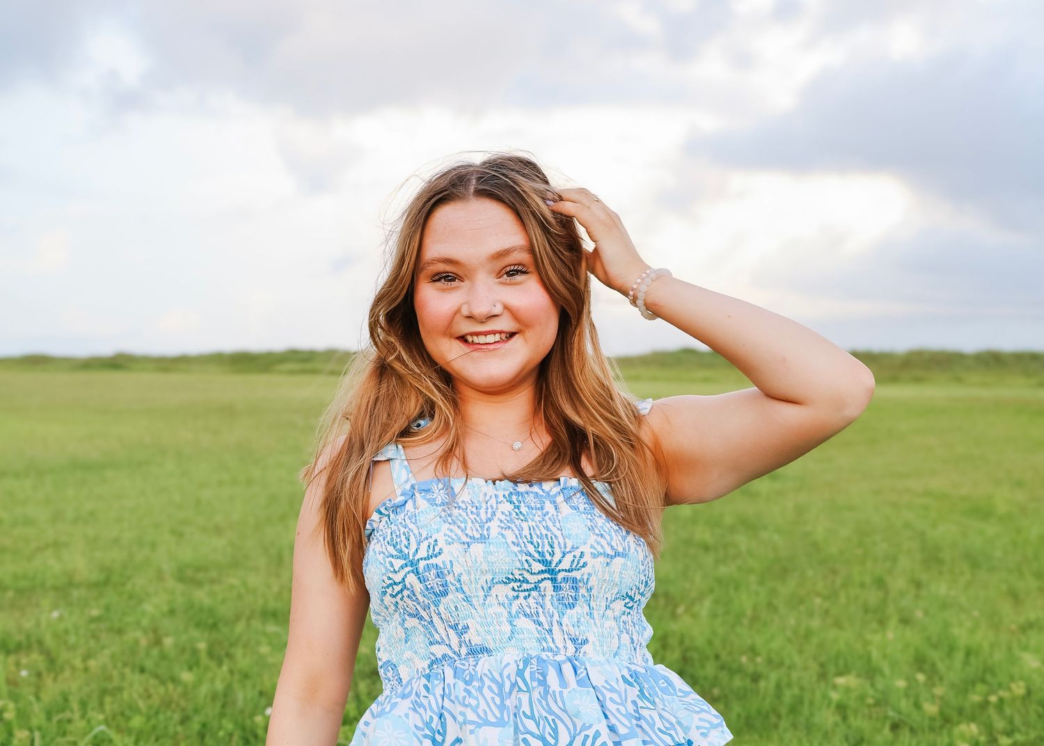 Candid summer portraits taken in a breezy green field under cloudy skies.