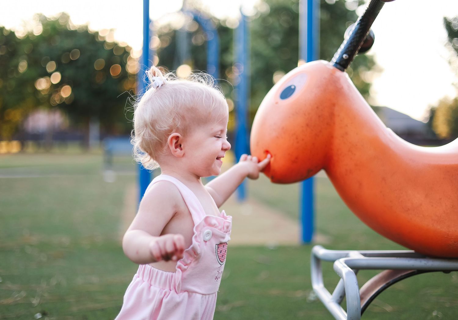Child playing on an orange horse-shaped playground spring rider at sunset.