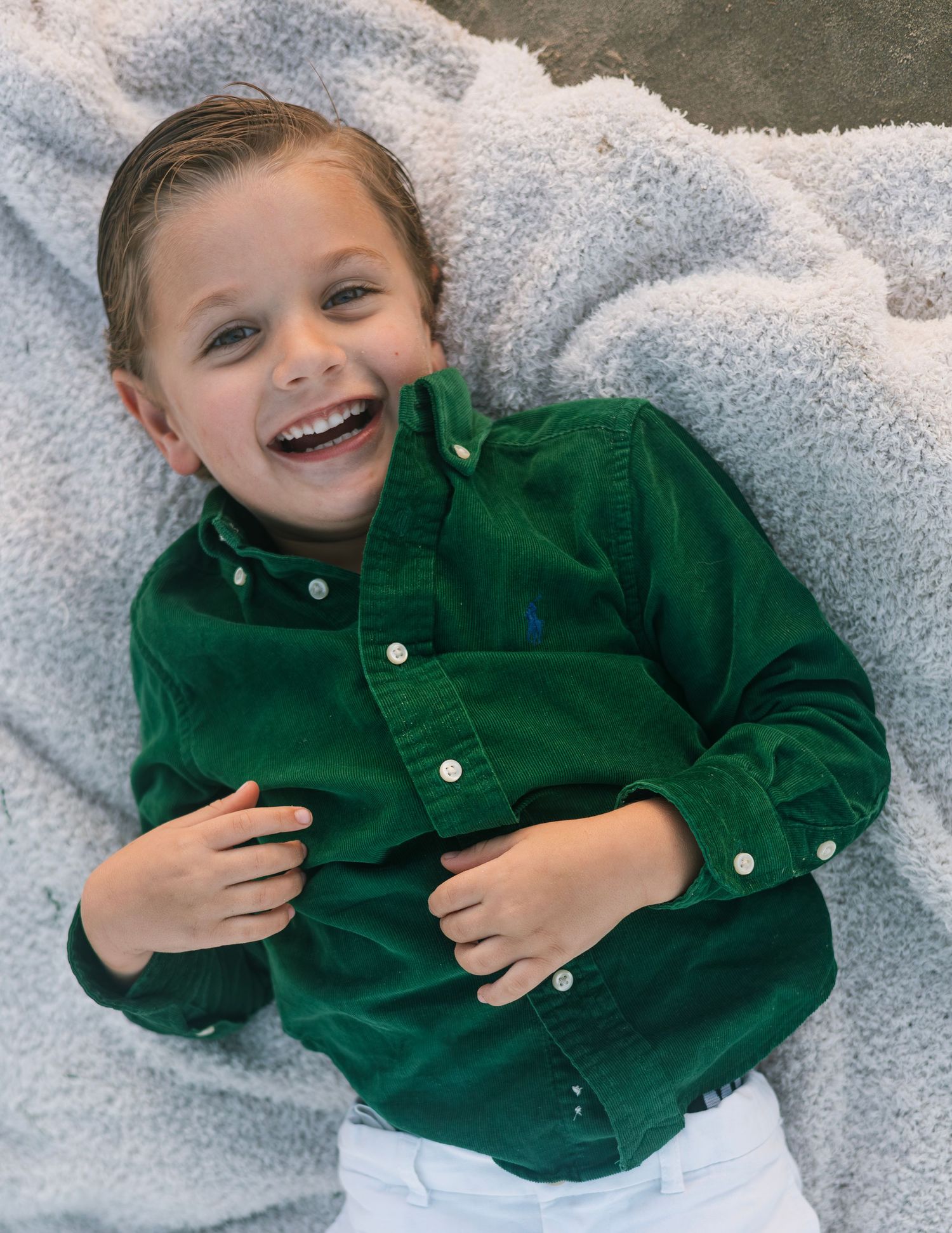 Child in green corduroy jacket lying on white surface showing playful expressions in sequence of photos.