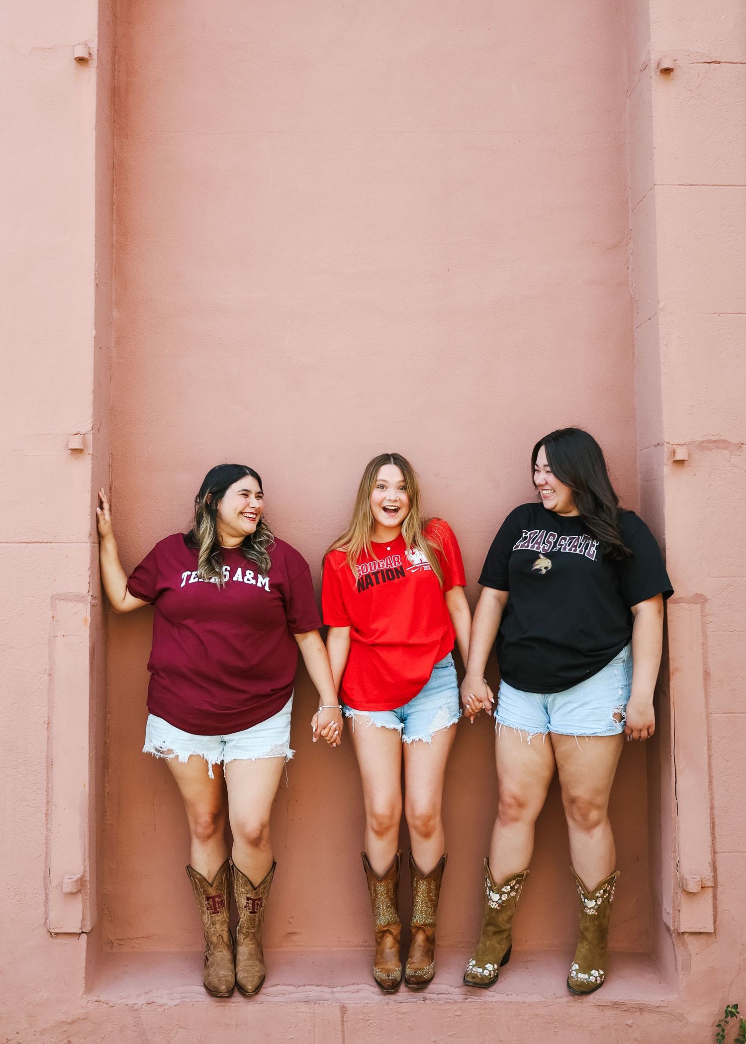 Group of friends in casual attire and cowboy boots posing against a pink wall.
