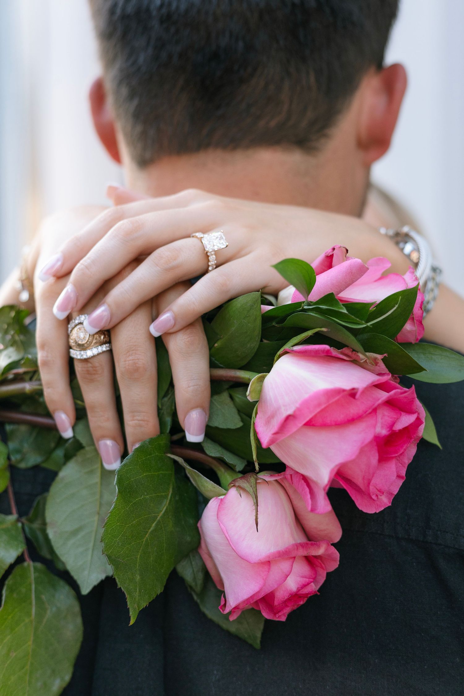 Pink roses and engagement ring detail shot against black clothing.