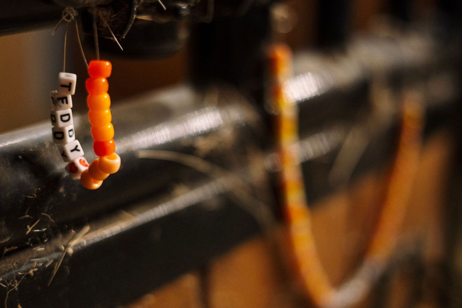 Colorful orange and yellow beaded bracelet with letter charms hanging from a dark metal surface.