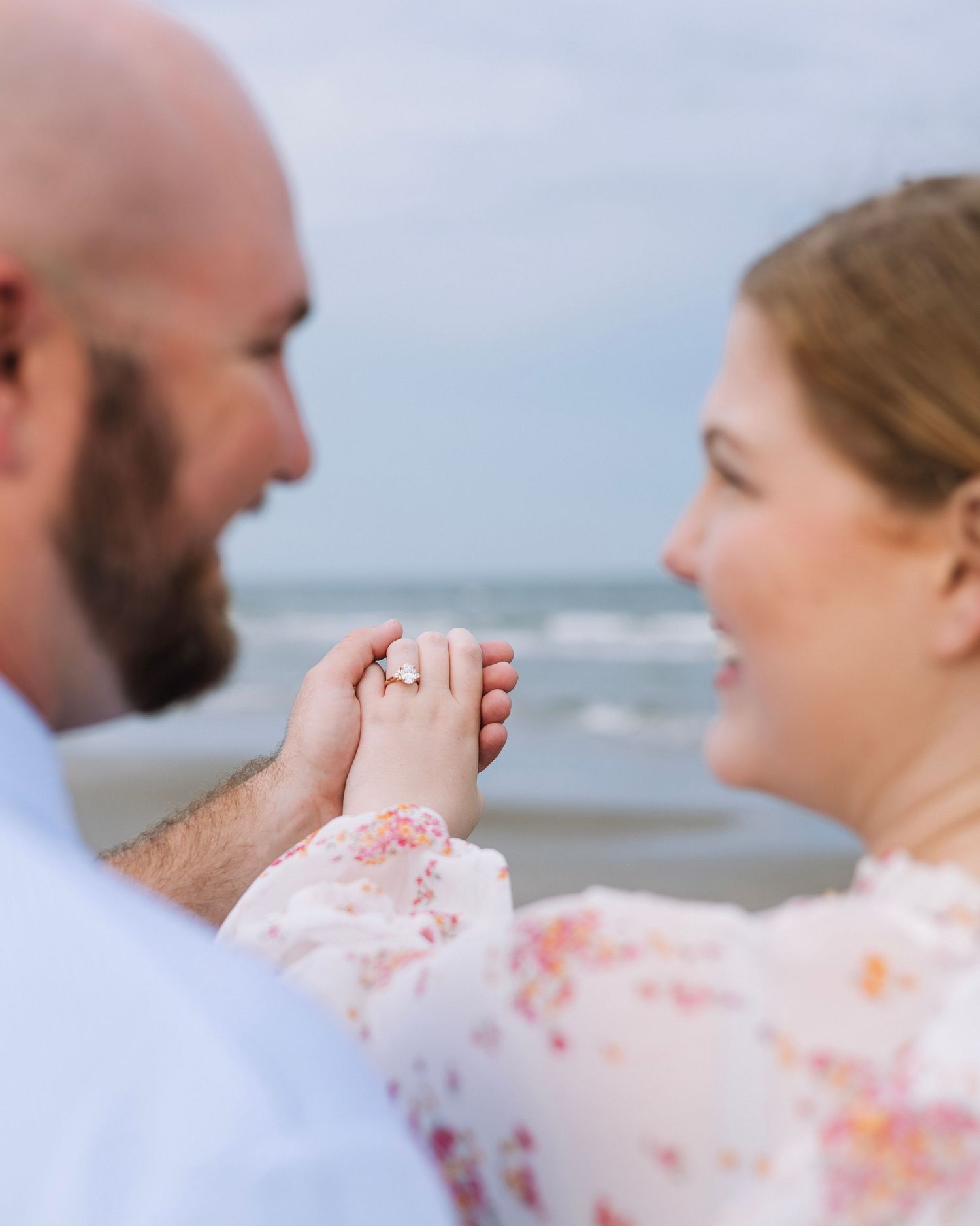 A couple shares a tender moment at the beach with the ocean waves in the background.