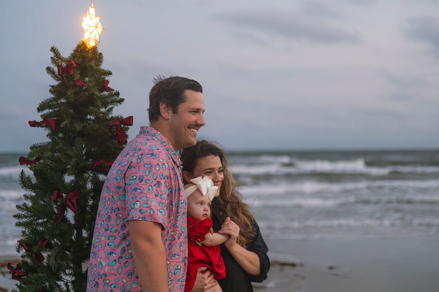 A couple in casual attire shares a tender moment while walking along a stormy beach at sunset.