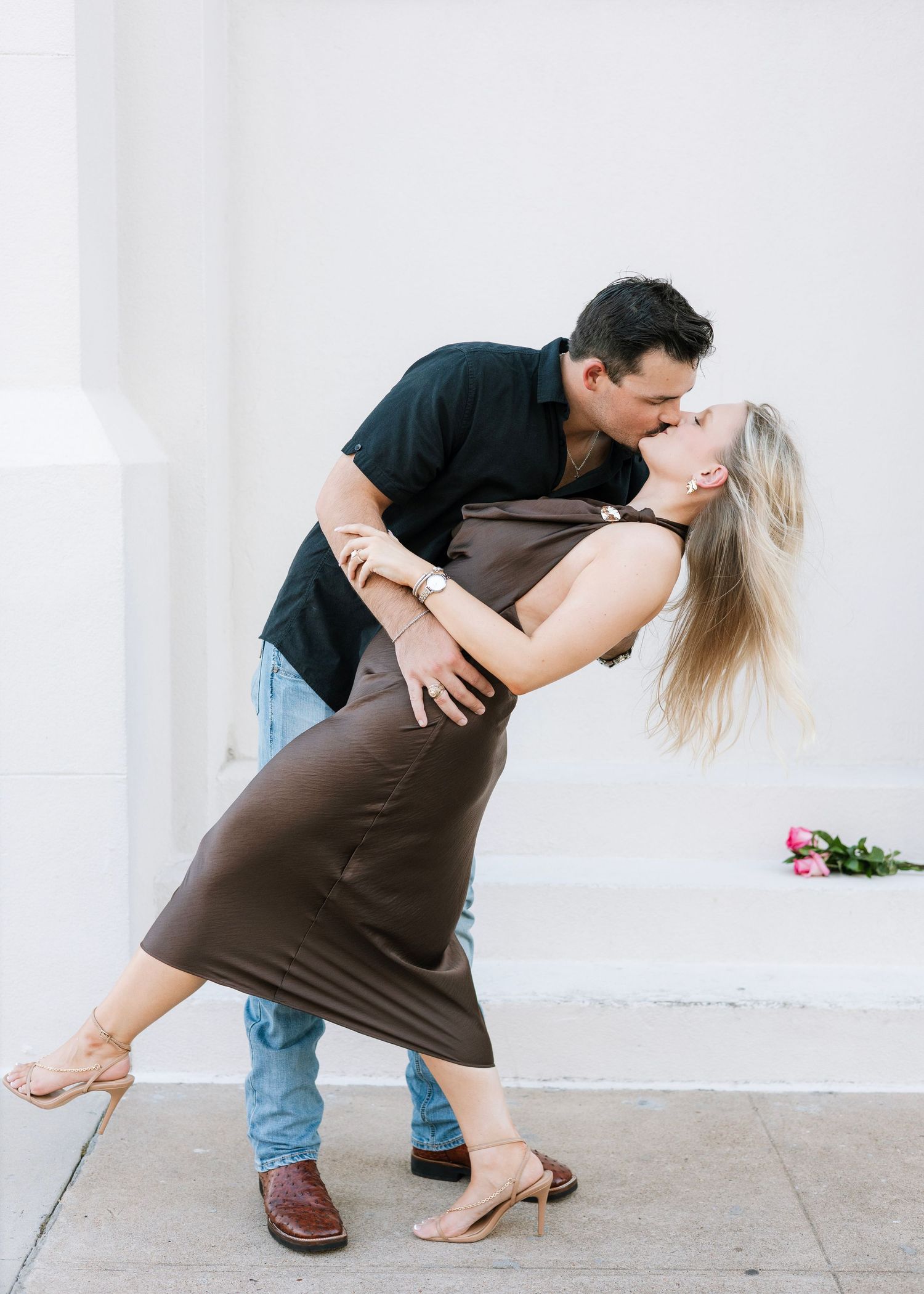 Couple in casual wear sharing an intimate dance pose against a white wall.