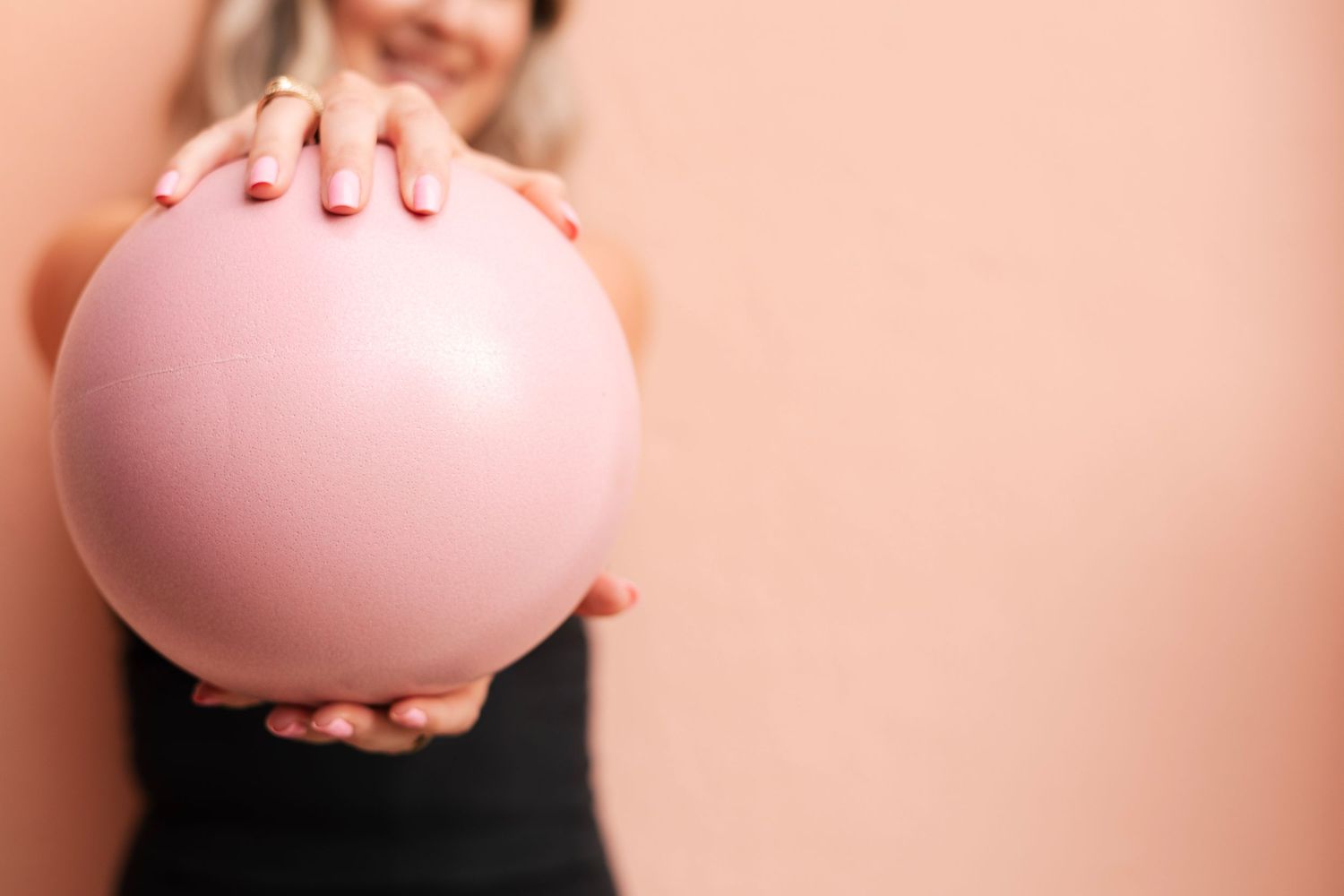 Woman holding a large pink balloon against a peach background, showcasing a fun and festive party atmosphere.