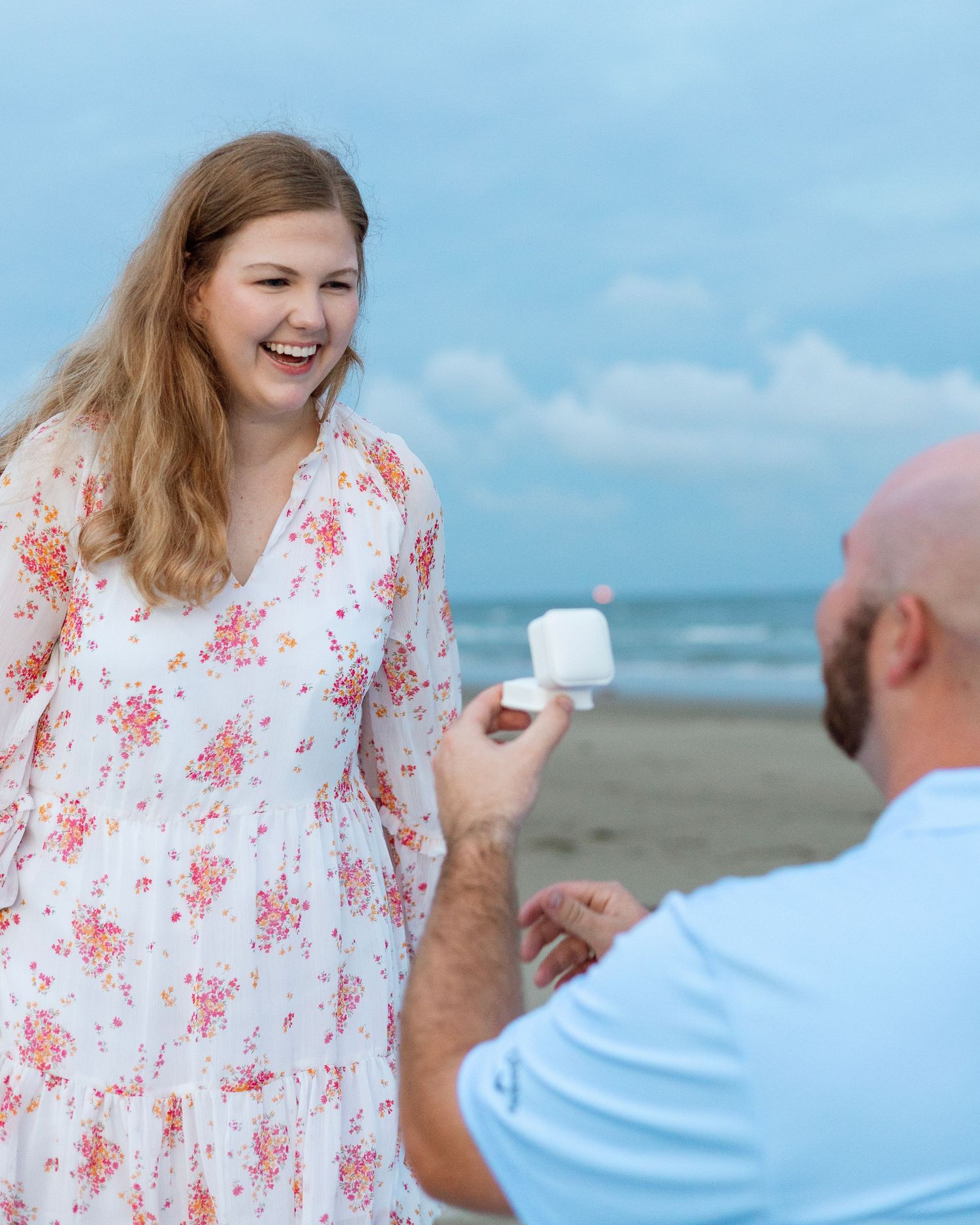 A couple shares joyful moments together on a beach with blue sky in the background.
