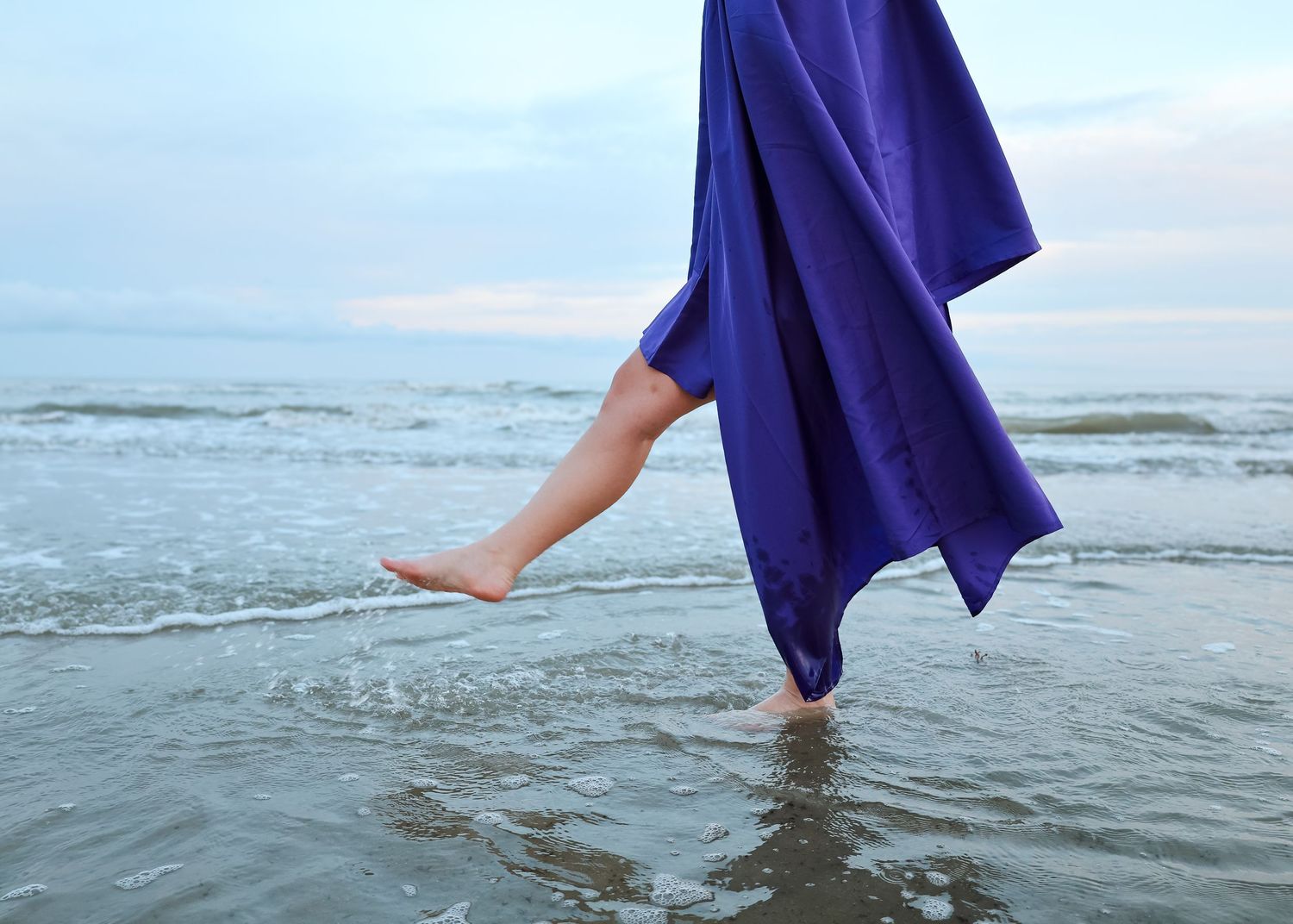 A series of photos showing someone walking into ocean waves while wearing a flowing navy blue dress.
