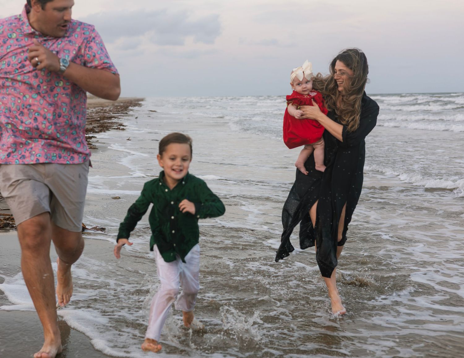 A family plays and splashes together in the shallow ocean waves at dusk.