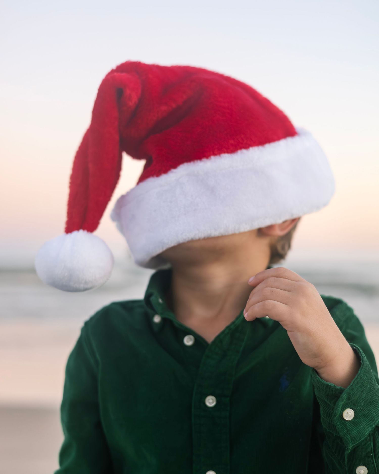 Row of red Santa hats against a light background with someone wearing a green shirt.