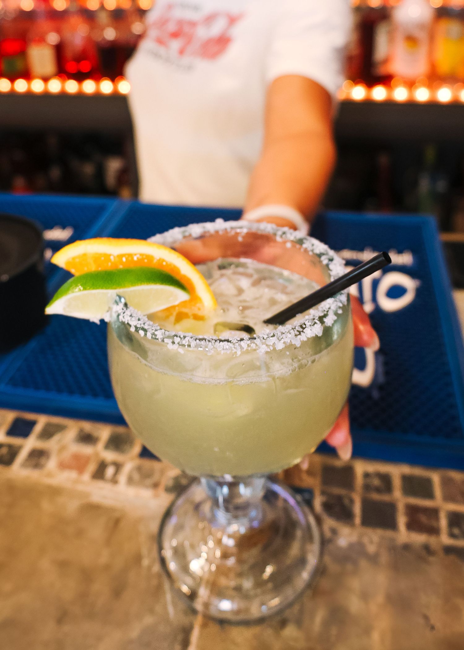 Row of margarita glasses with salted rims and lime garnishes on blue bar counter.