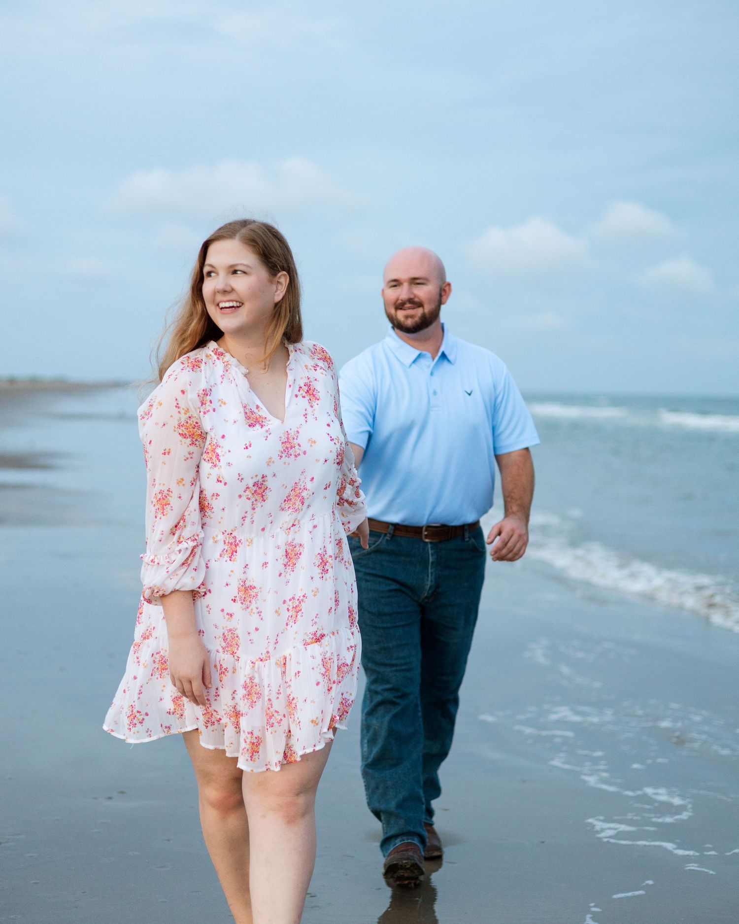 A couple walks along the beach shoreline wearing coordinated blue and floral outfits.