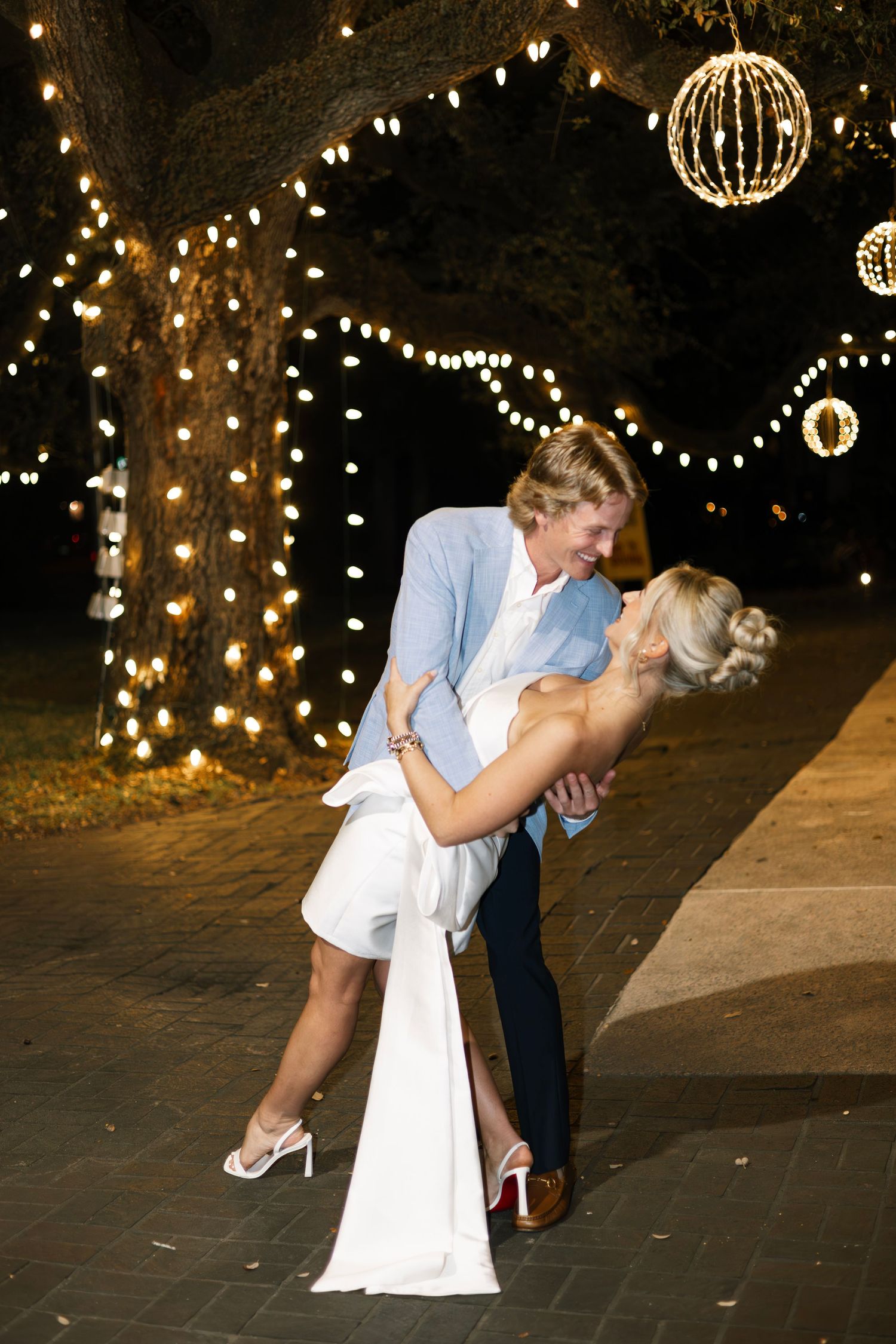 A romantic dance scene at night under glowing orb lights and string lights creating a magical outdoor atmosphere.