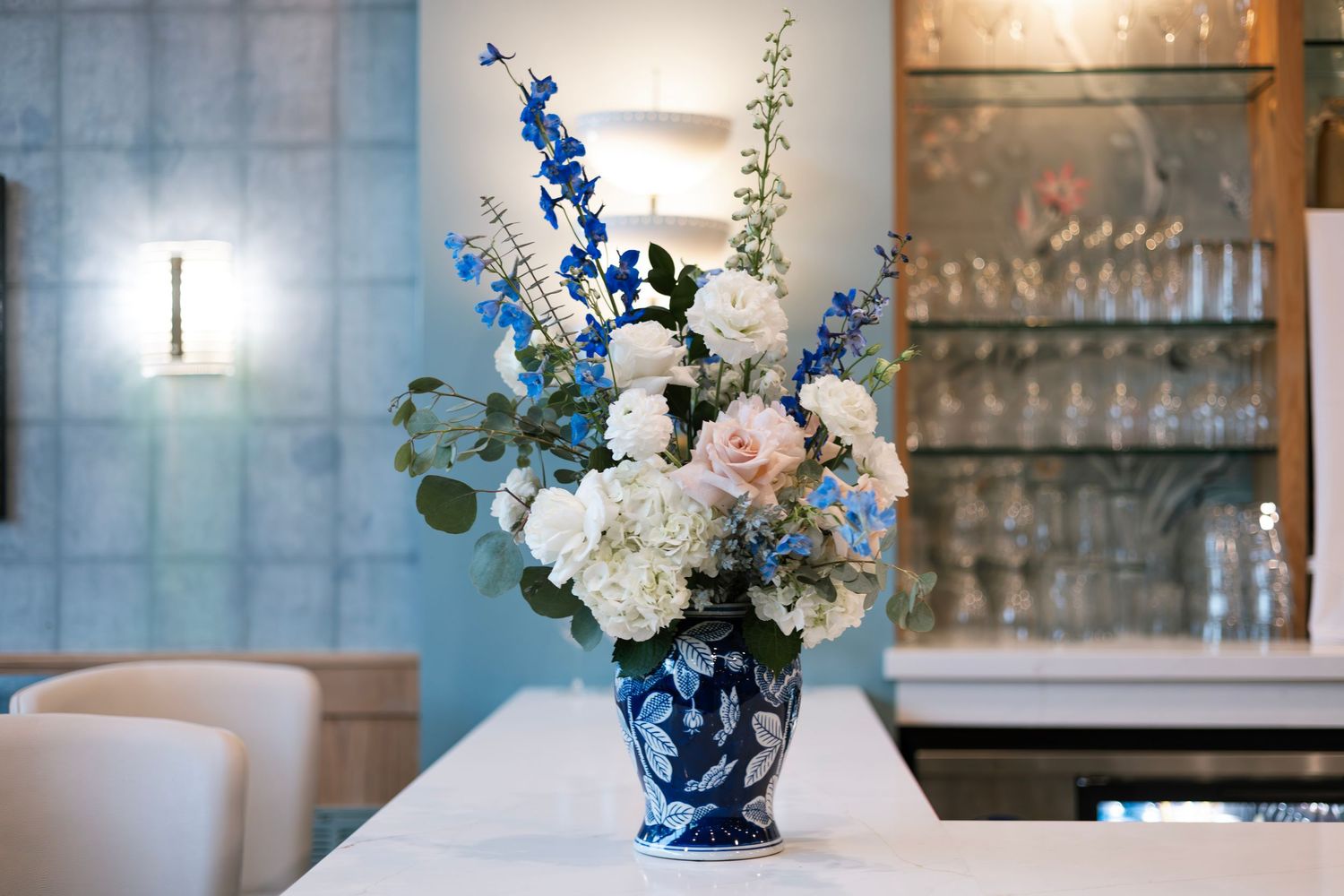 White floral arrangements in blue and white vases displayed on tables with glassware.