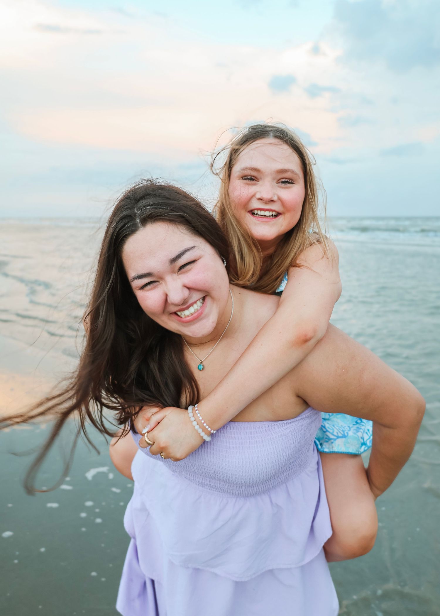 Friends sharing playful piggyback rides along a sunny beach shore.