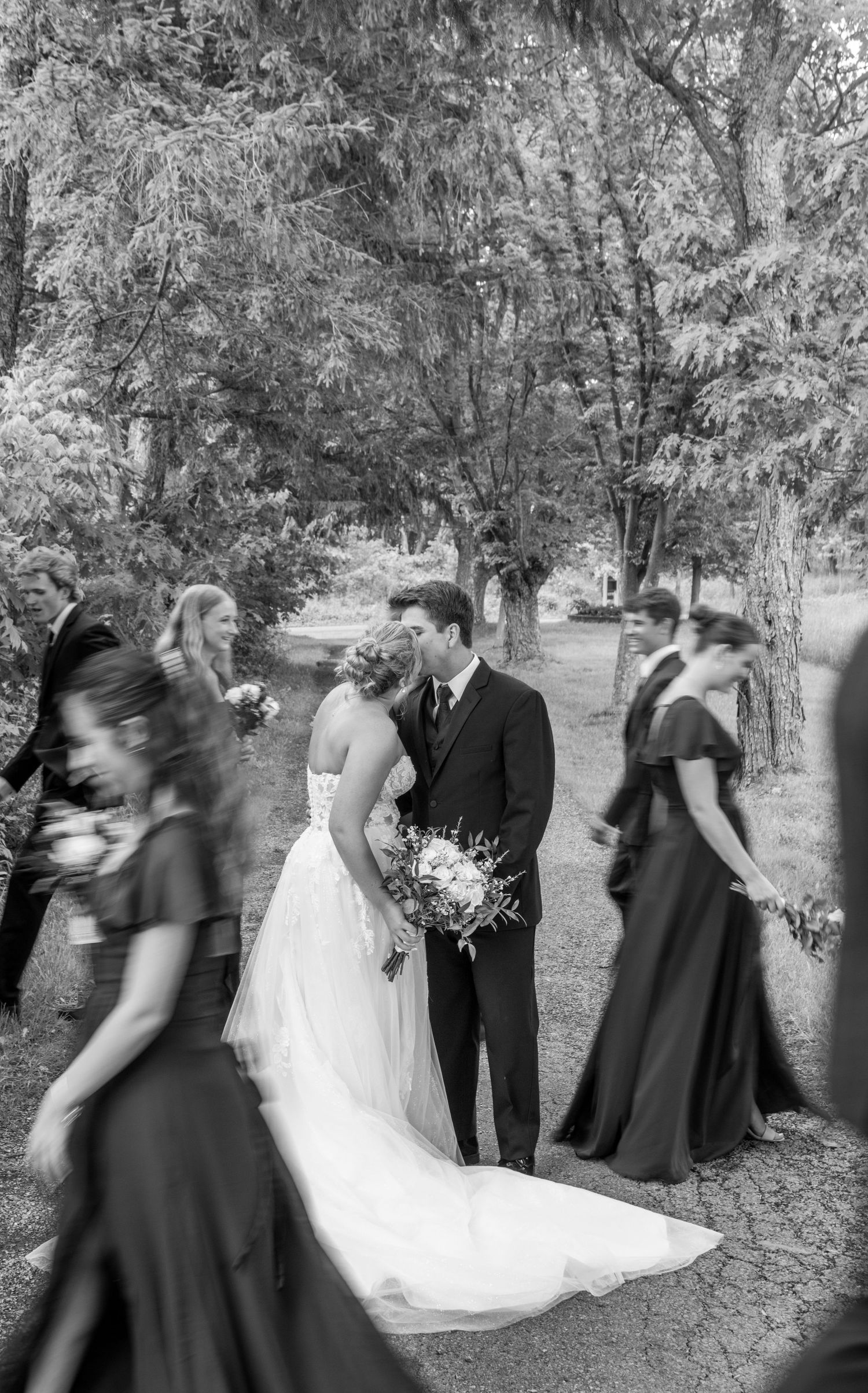 bride and groom kiss as bridal party walk pass
