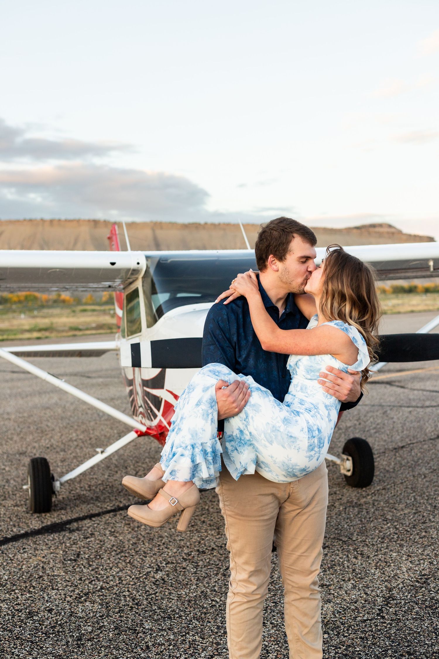 man lifts fiance and kisses her in front of small airplane